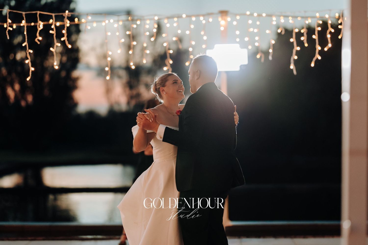 Newlyweds share a romantic dance under twinkling string lights at their evening wedding reception.