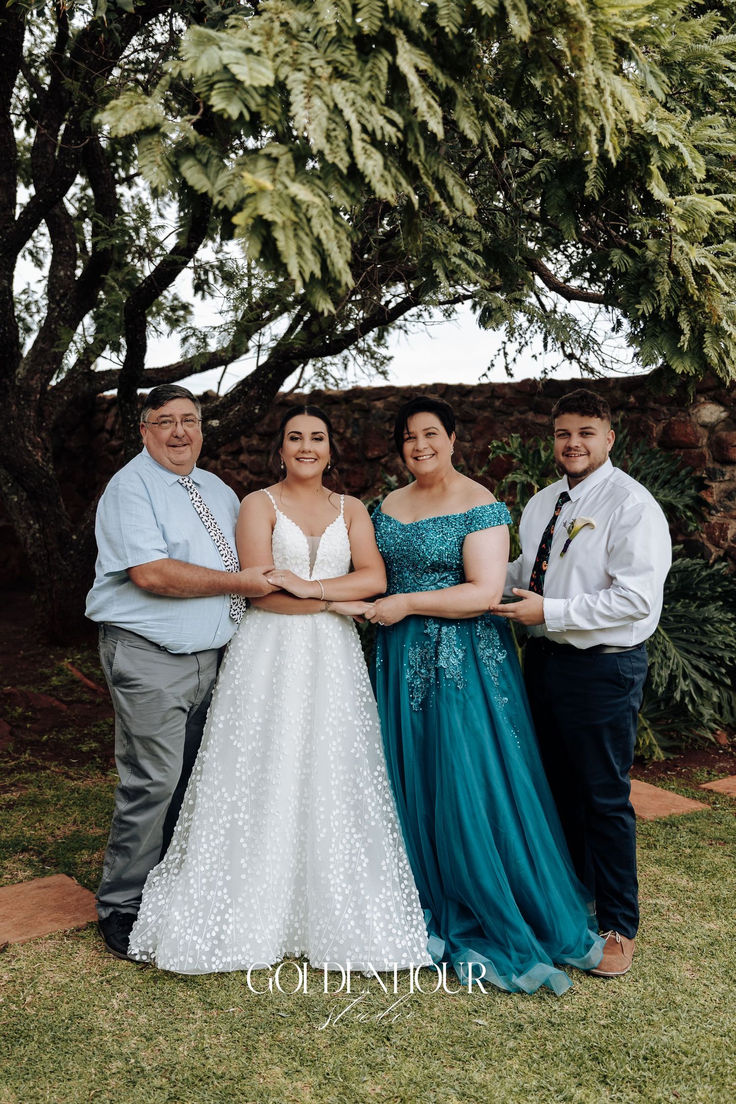 Wedding party in teal and white attire posed together under a large tree.