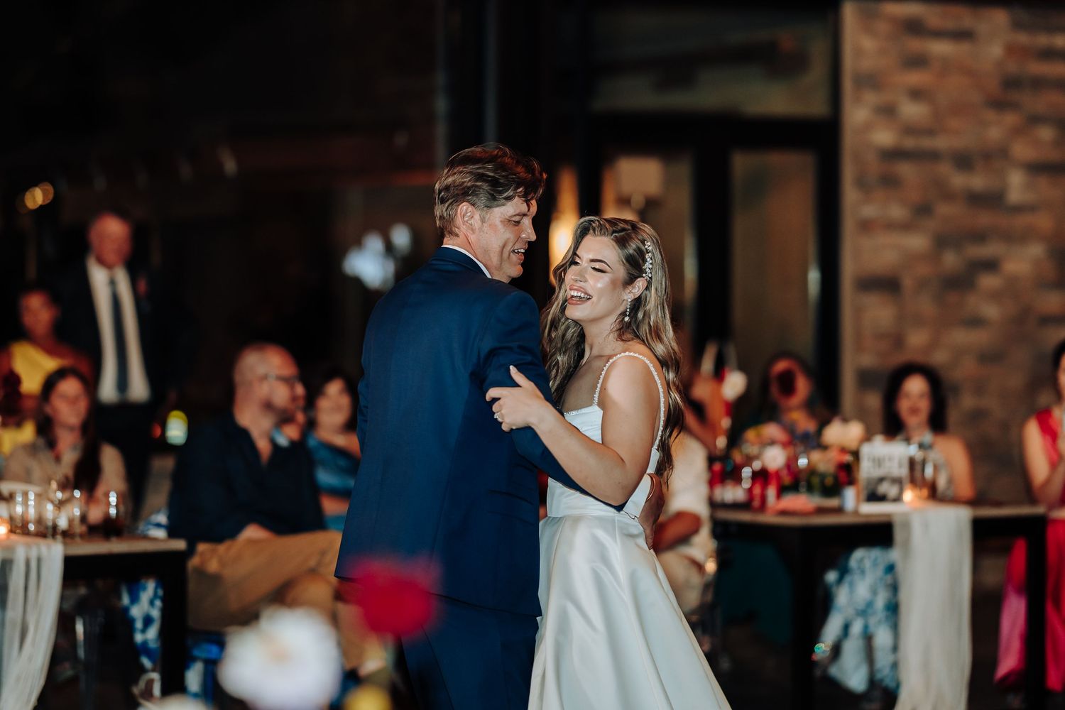 Couples slow dancing at an evening wedding reception with atmospheric lighting.