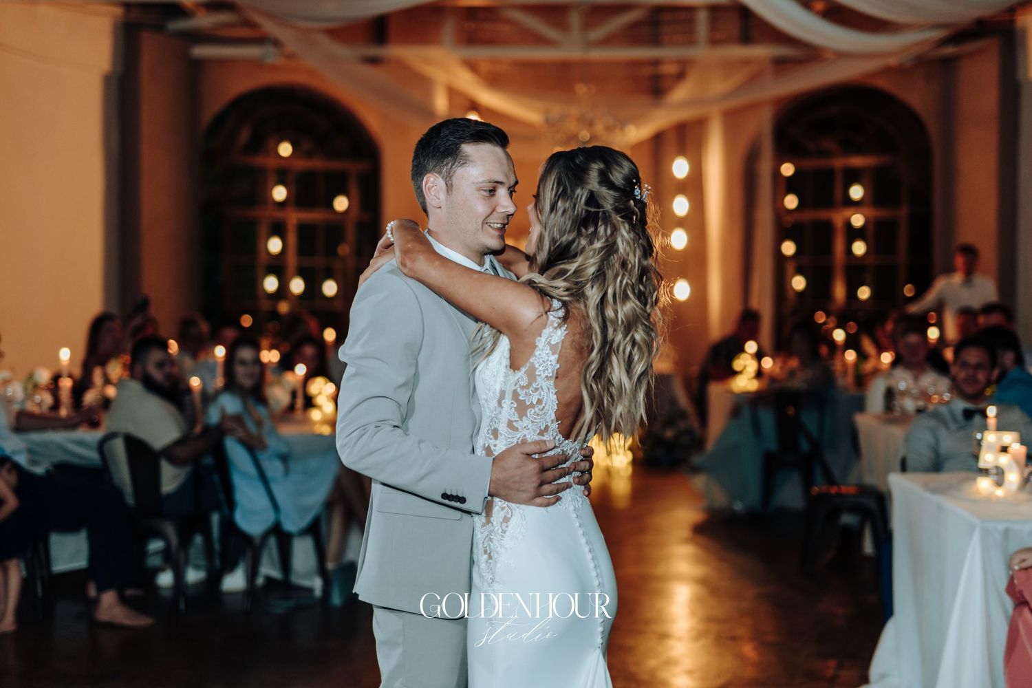 A romantic first dance in a warmly lit reception venue with string lights.