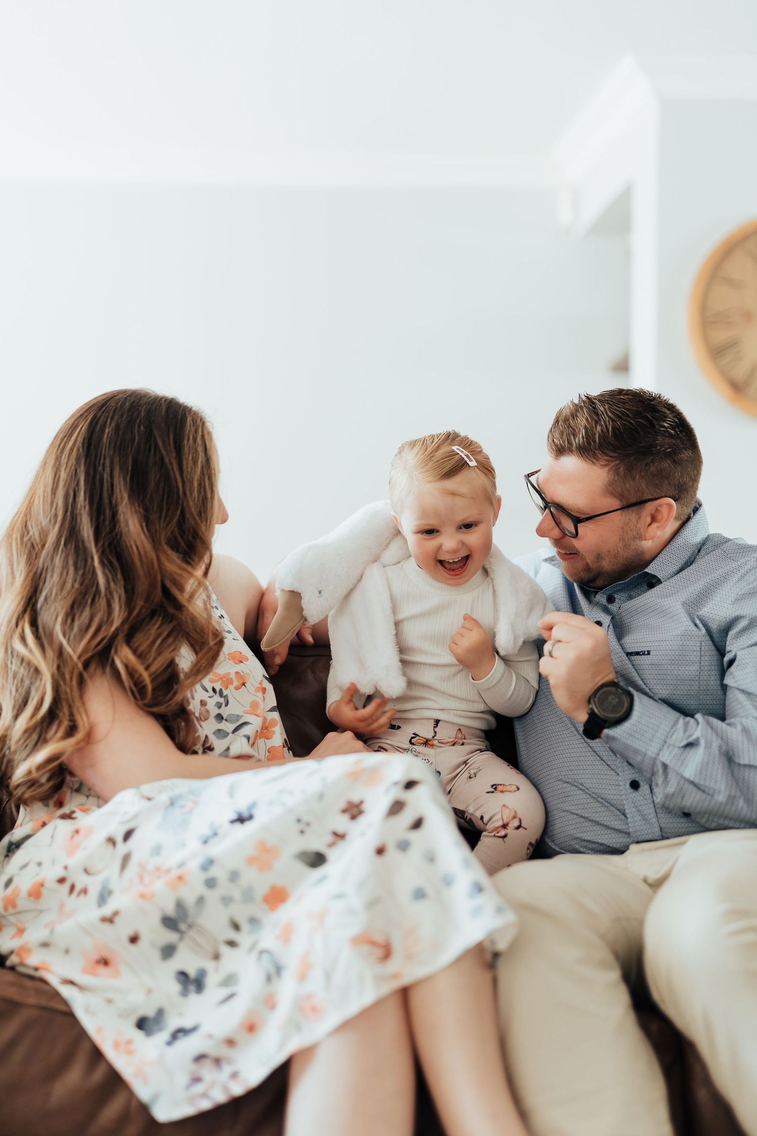 Intimate family photo series showing playful candid moments together on a white bed with floral bedding.