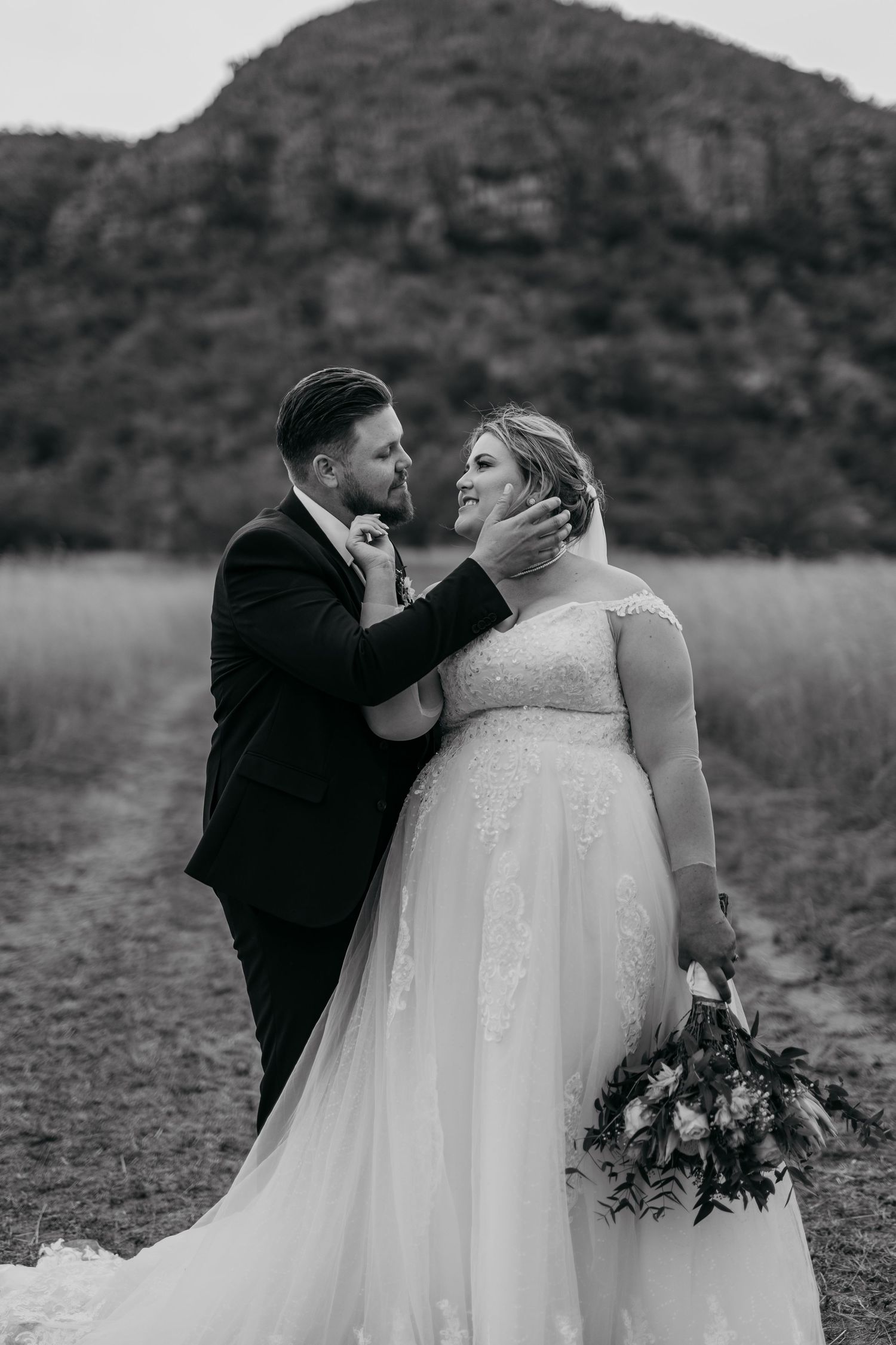 A tender wedding moment captured in black and white against a mountainous backdrop, with a beautiful bouquet in hand.