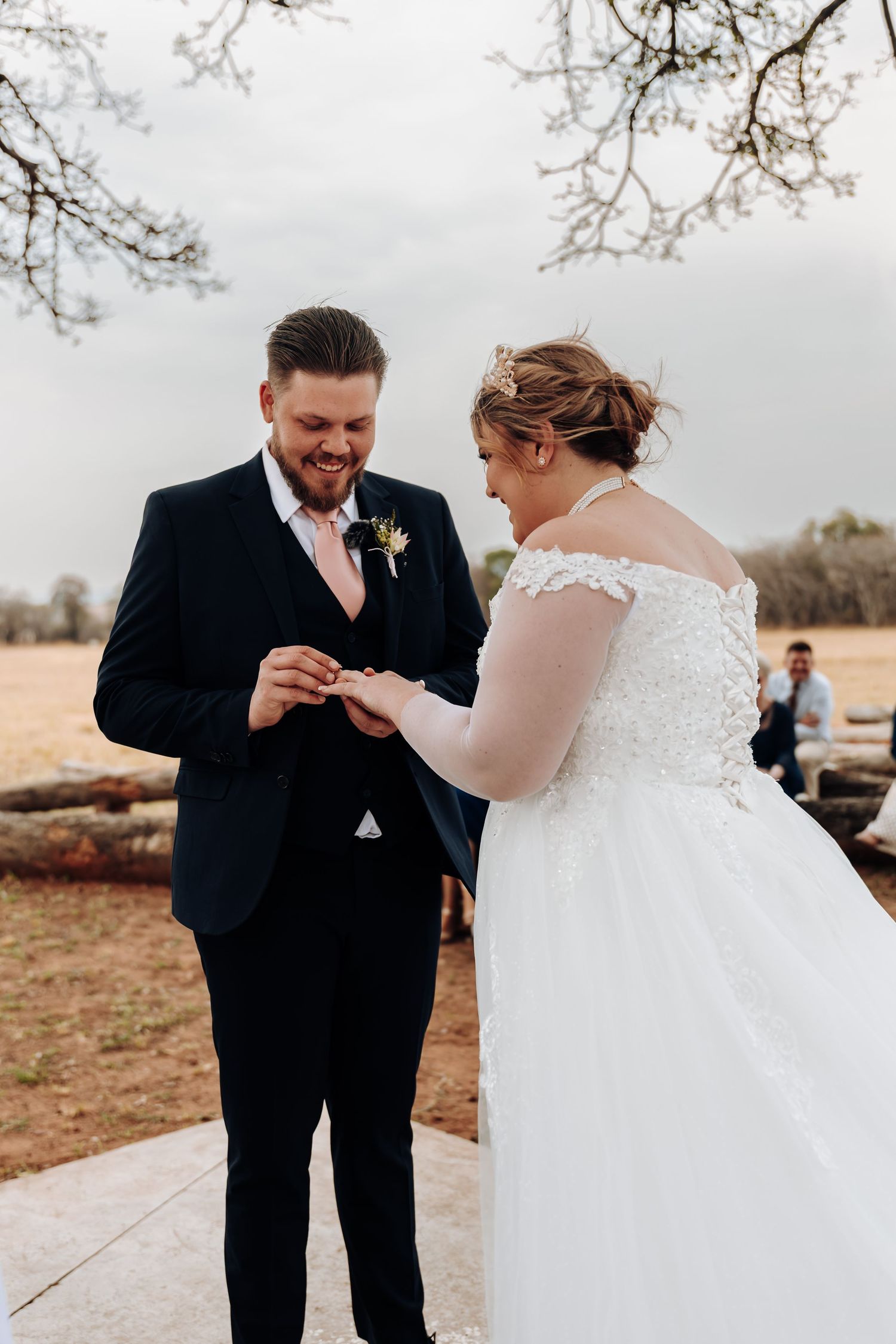 A couple exchanges rings during an outdoor wedding ceremony on a cloudy day.