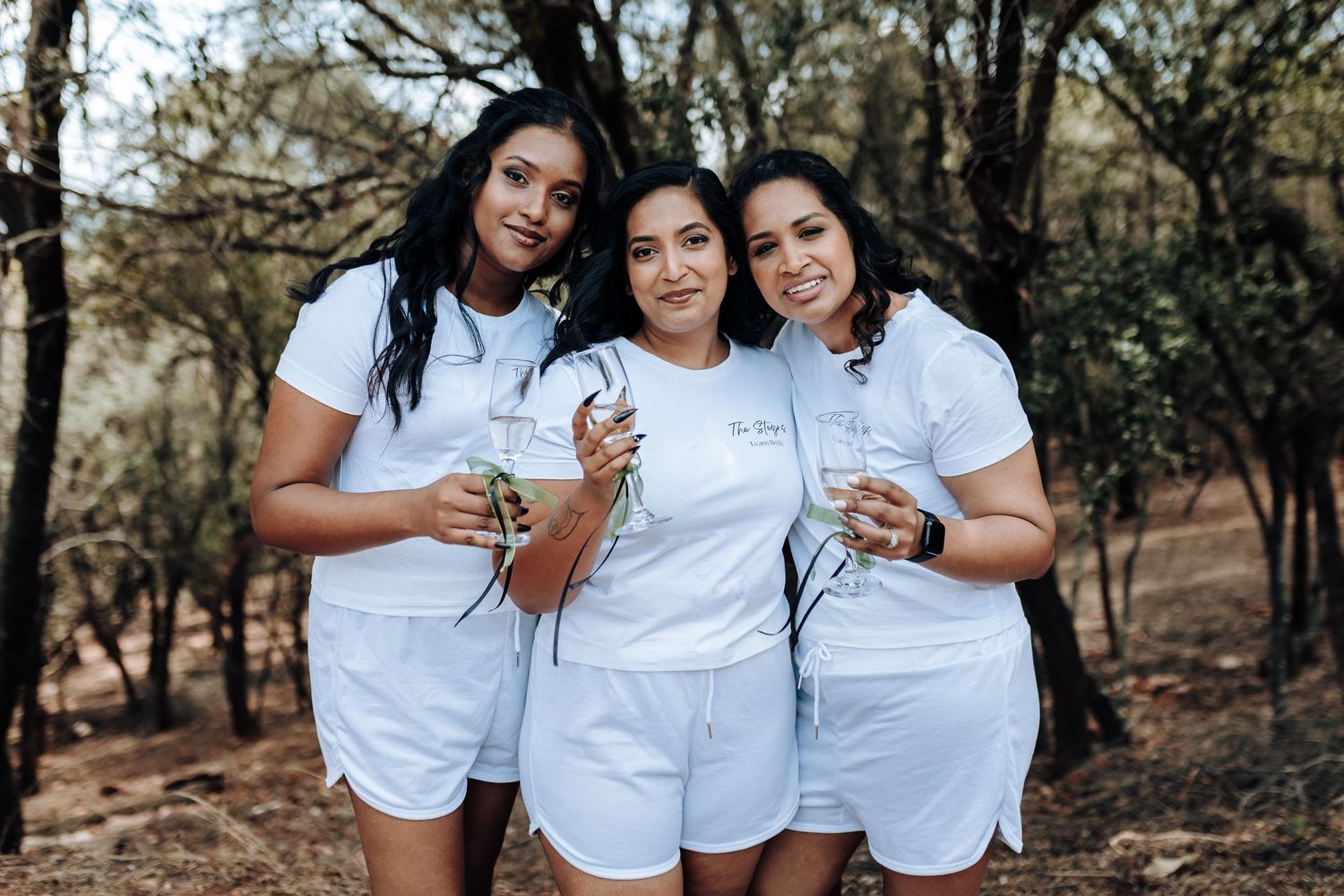 Group wearing matching white outfits celebrating outdoors with champagne glasses.