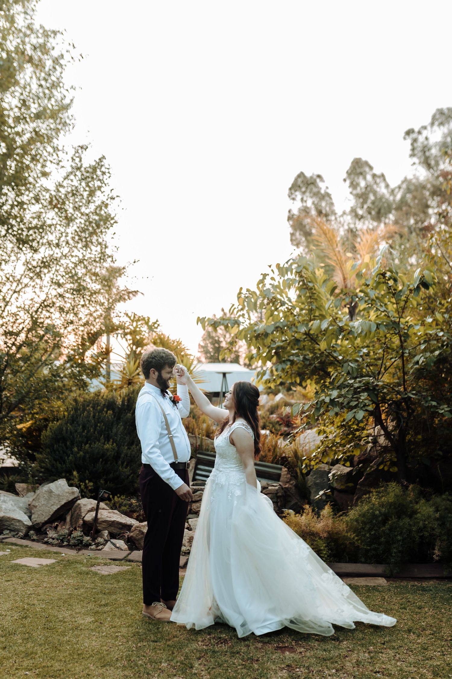 Candid wedding moment of couple dancing together in garden during sunset.