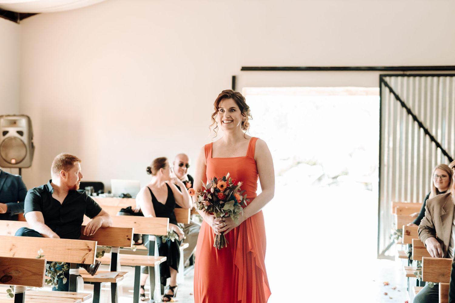 Bridesmaid in coral dress carries floral bouquet during wedding processional.