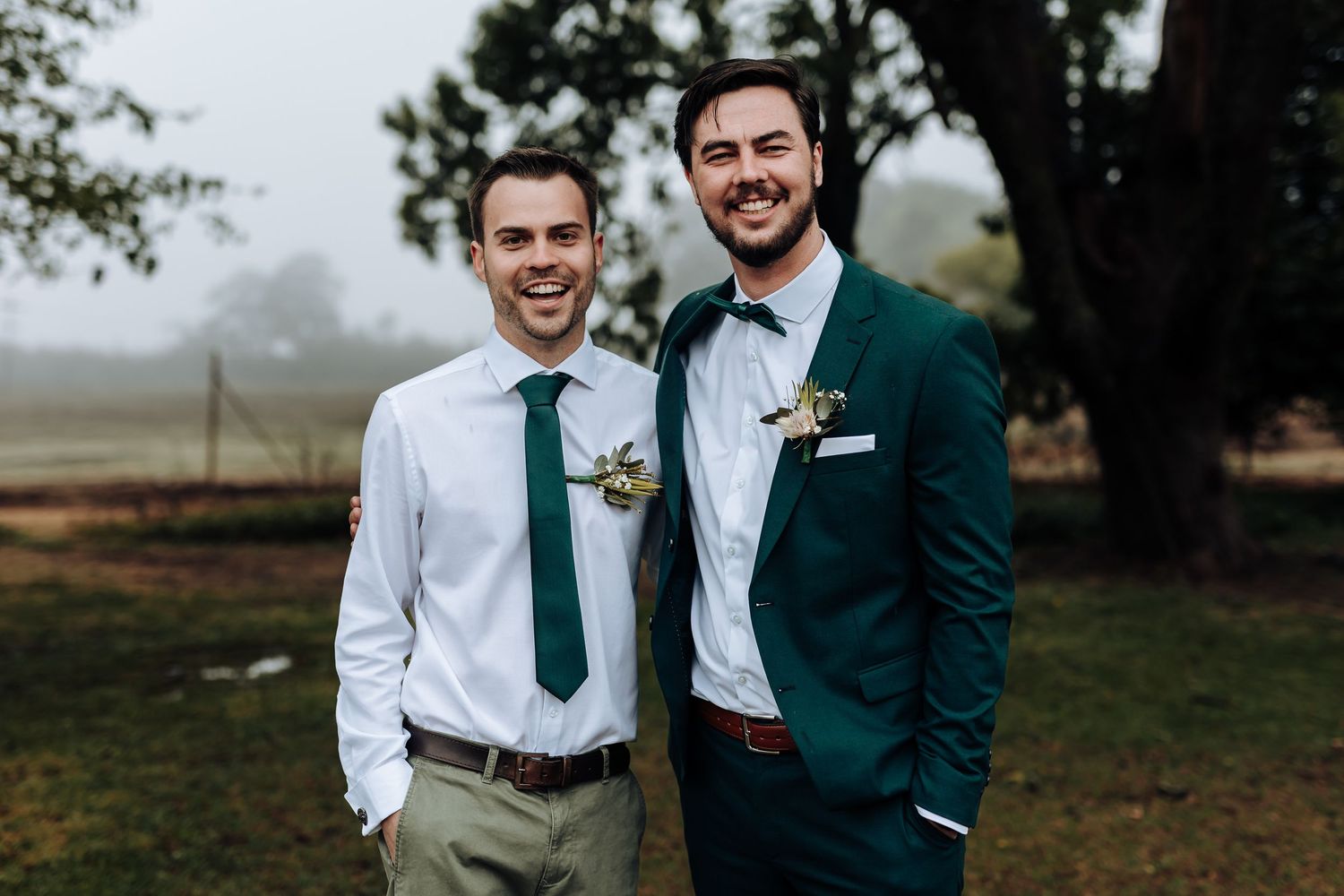 Wedding party members pose together outdoors wearing coordinating emerald green and white attire.