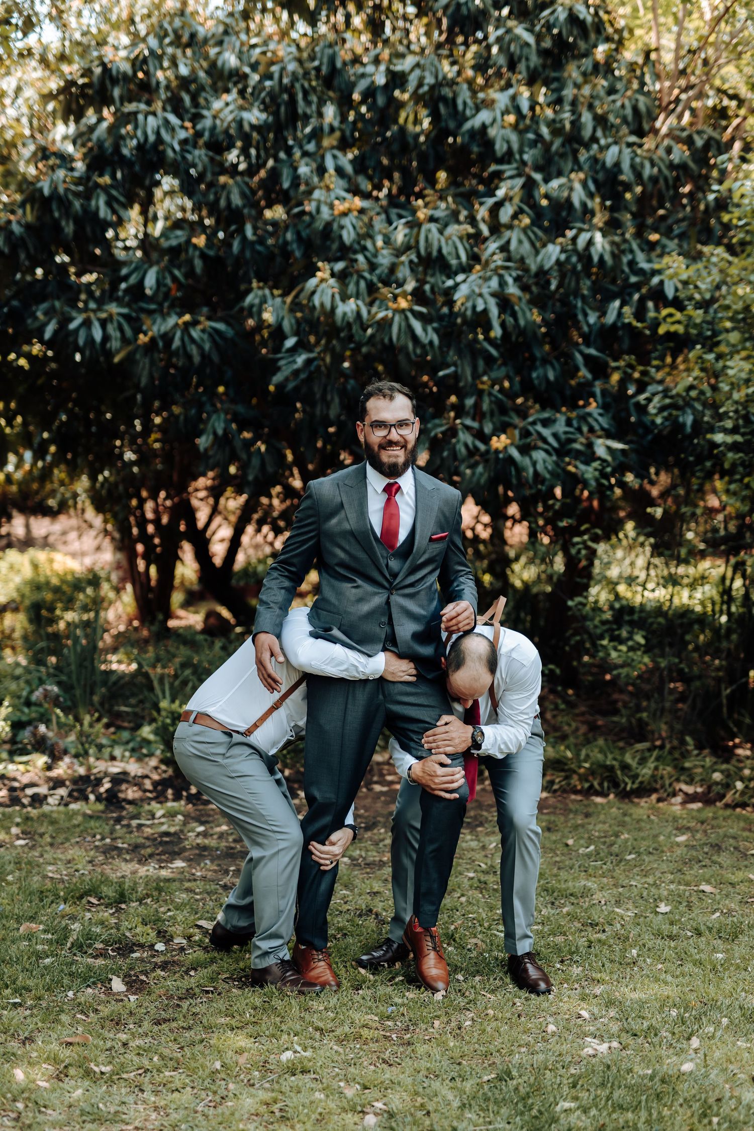 Fun wedding party photo showing groomsmen pretending to tackle the man in the dark suit.