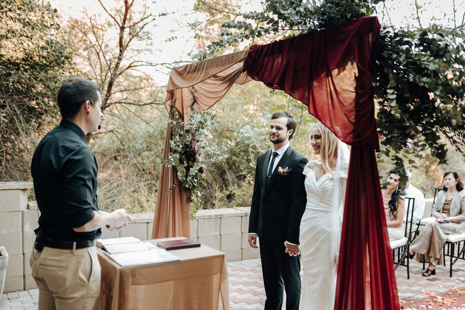 A wedding ceremony taking place at an outdoor venue with draped decor.