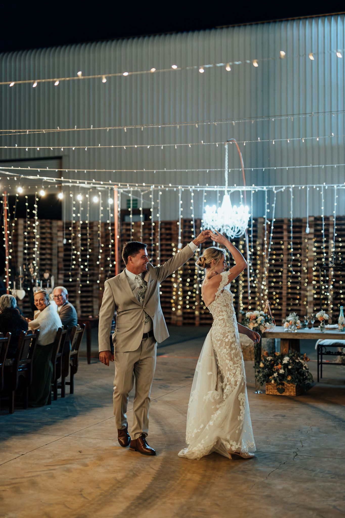 Couple dancing beneath elegant string lights at an indoor wedding reception.
