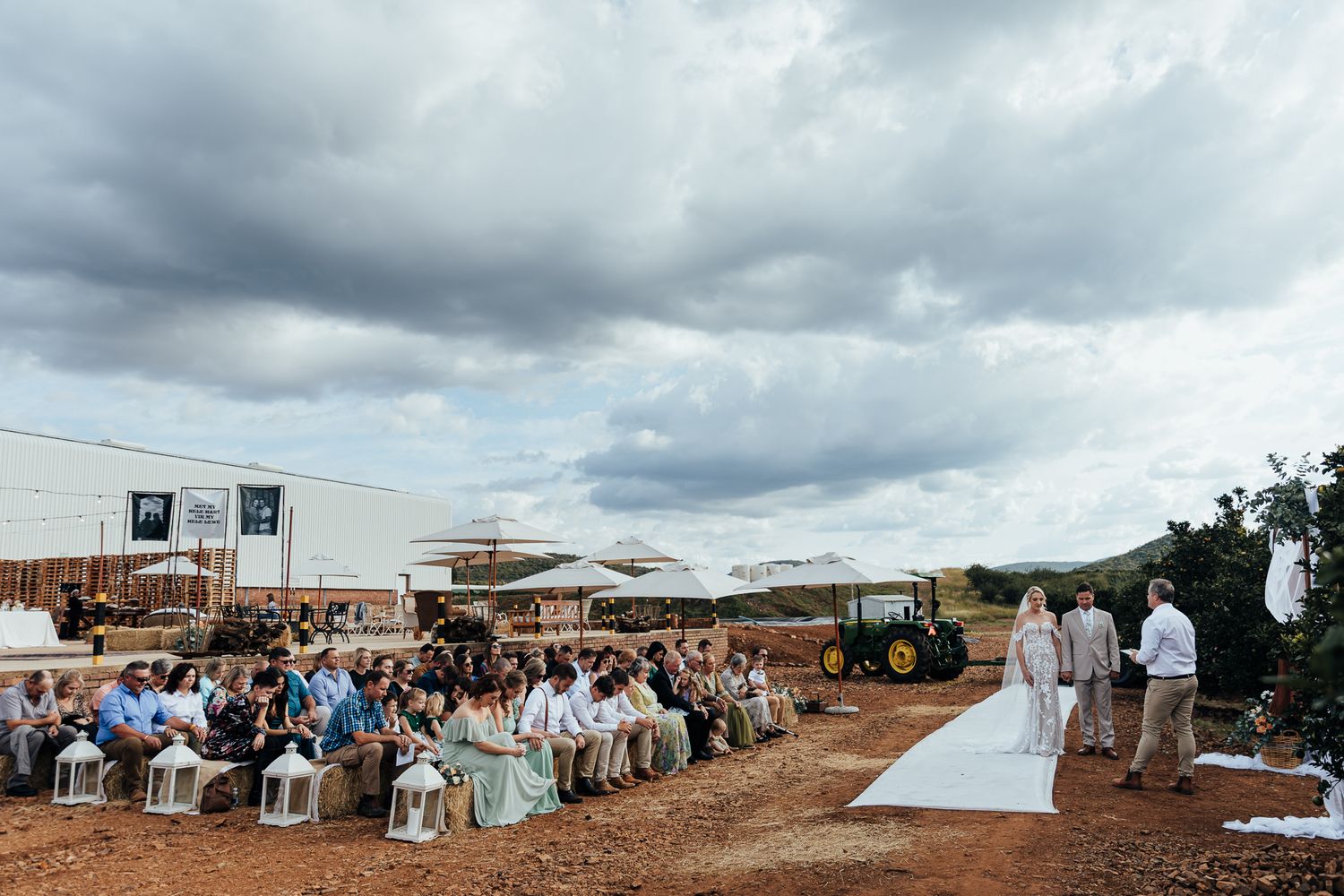 Wide view of rustic outdoor wedding ceremony with guests seated on white chairs.