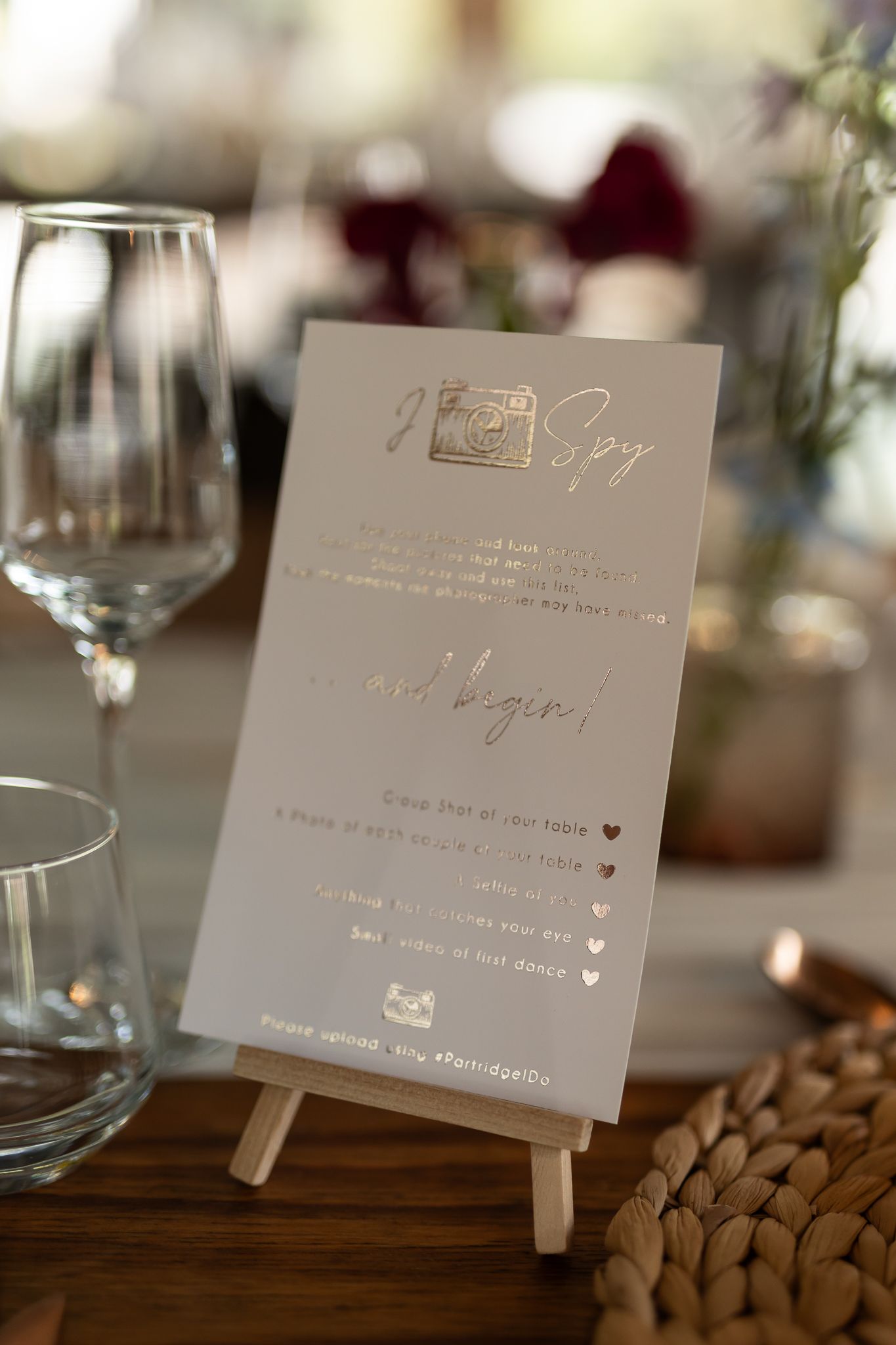 Wedding menu card displayed on small easel with wine glasses and rustic table decor.