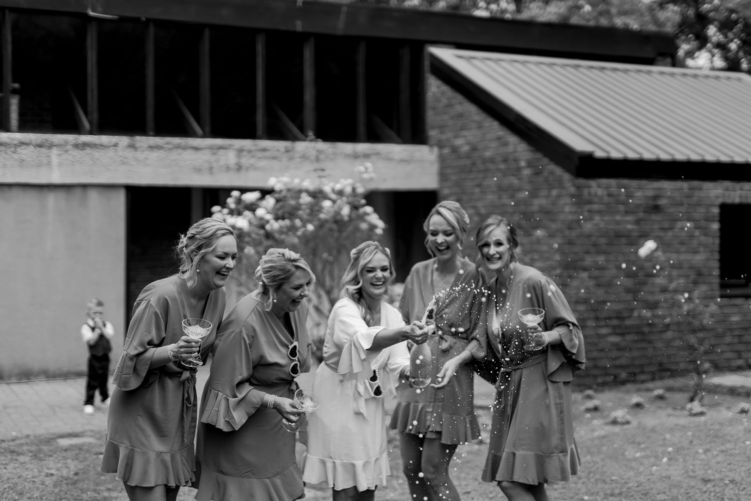 Black and white photo of a bridal party in matching robes laughing together outdoors.