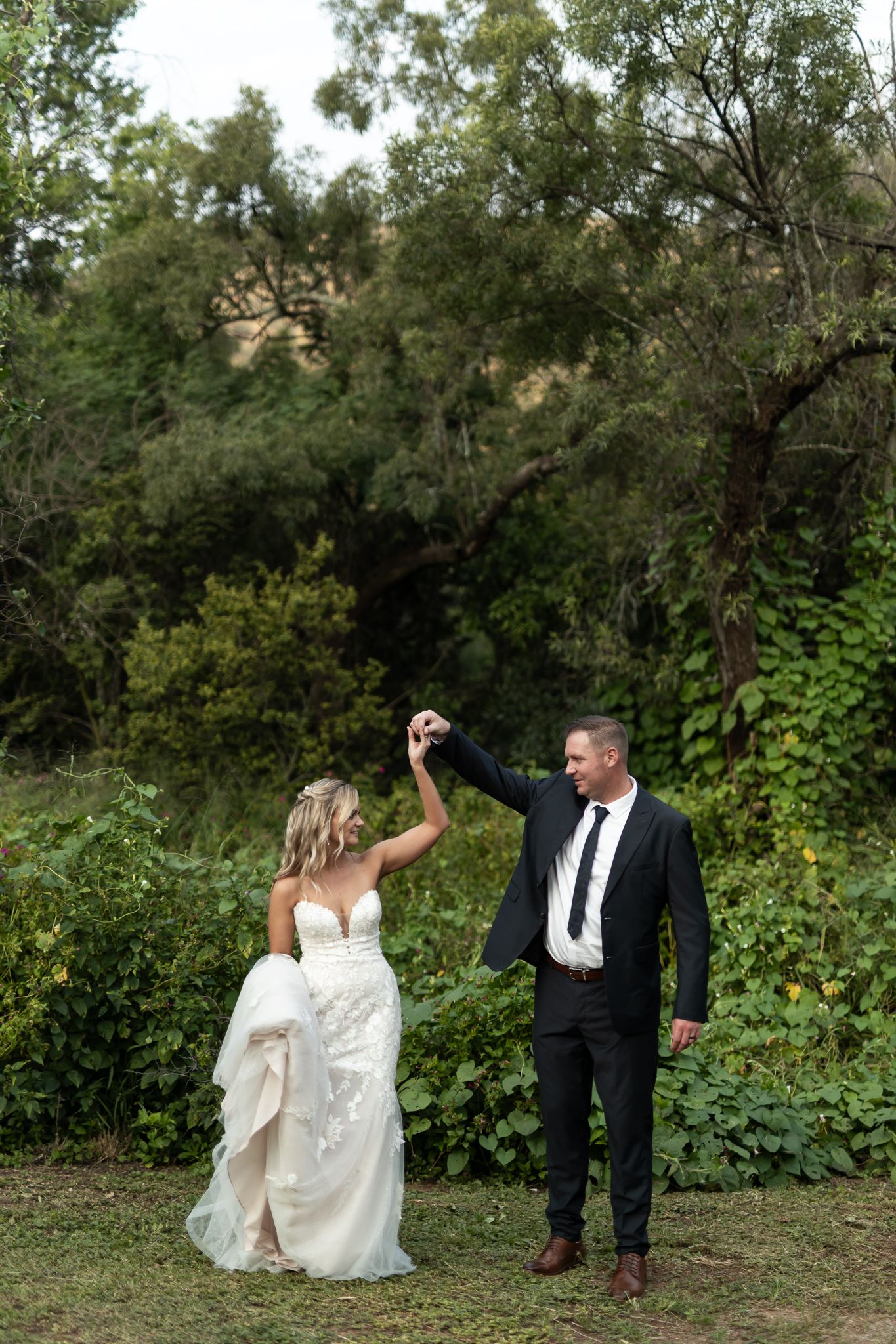 A couple dances together on a dirt path surrounded by lush greenery and trees.