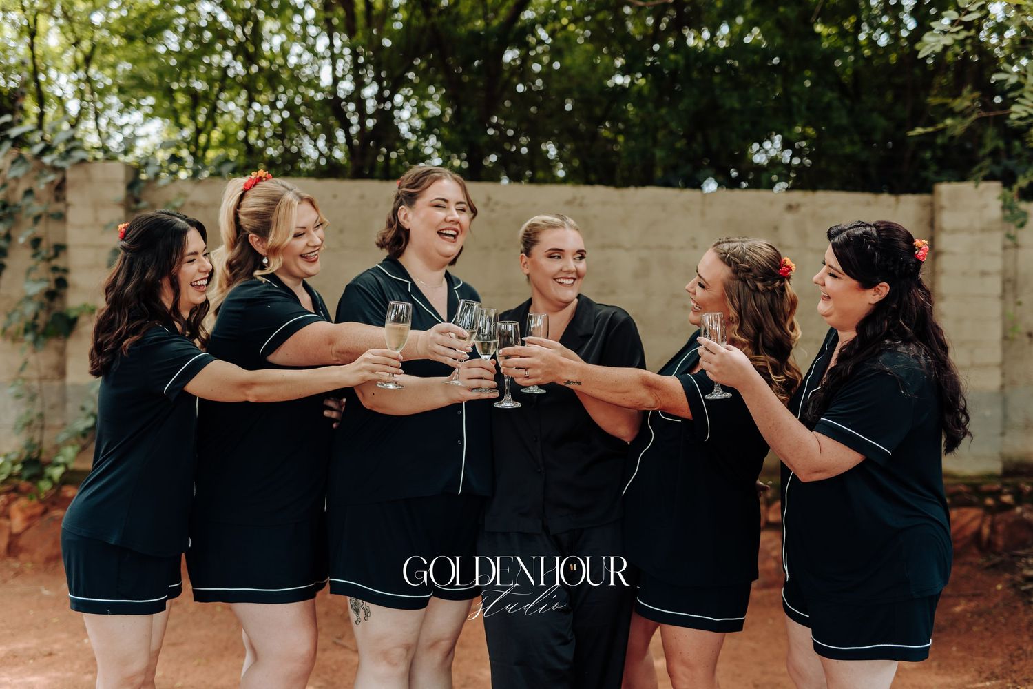 A group of women in matching black outfits toasting and celebrating together outdoors.