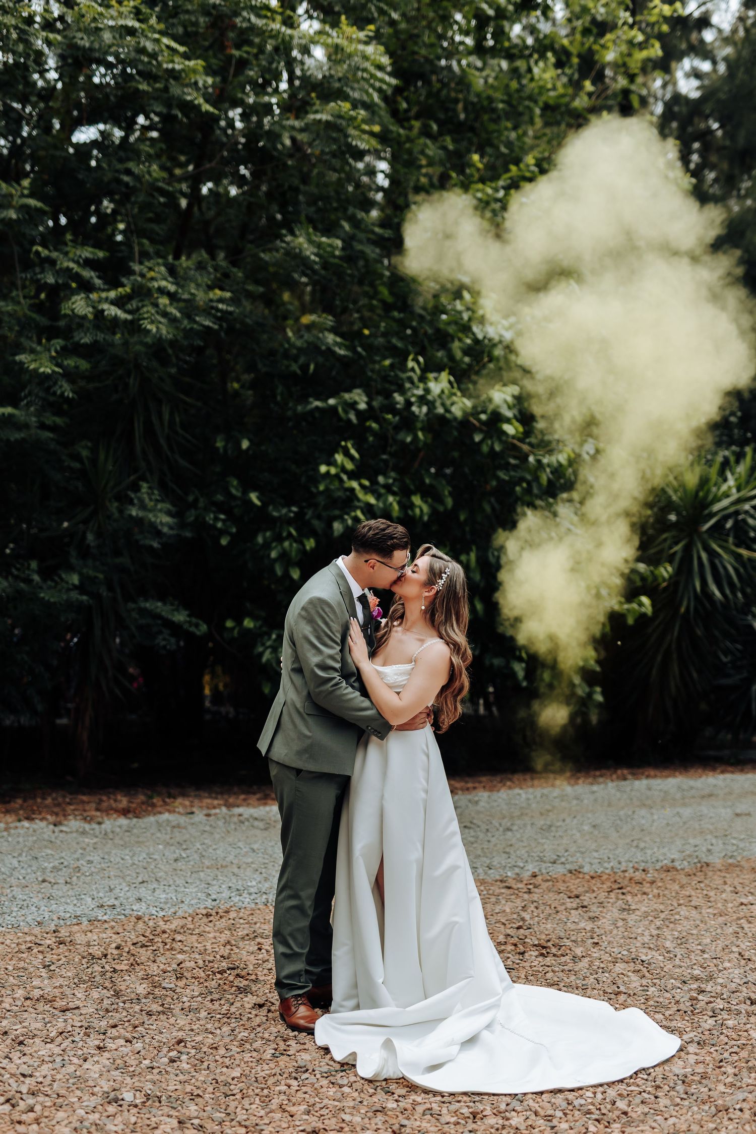 A wedding couple sharing an intimate moment with yellow smoke effects in a lush garden setting.