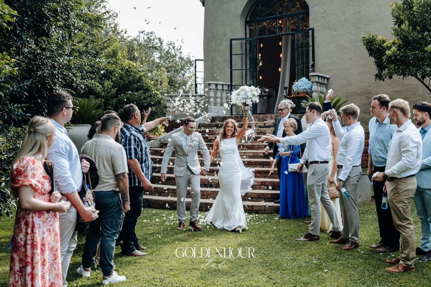 Wedding guests form two lines on a lawn as newlyweds celebrate outside a white church building.