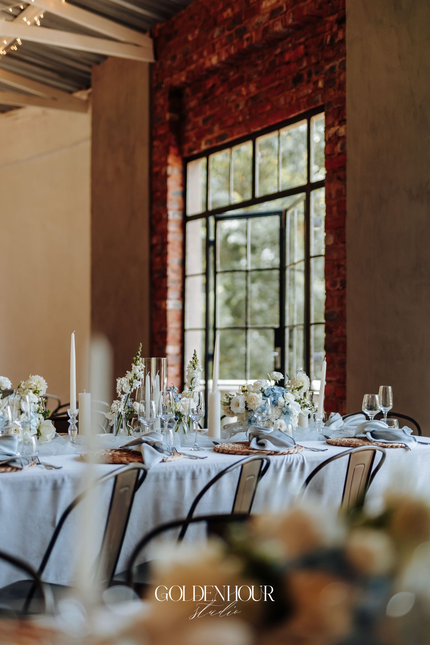 Elegant wedding reception tables set with white linens and floral centerpieces against exposed brick walls.