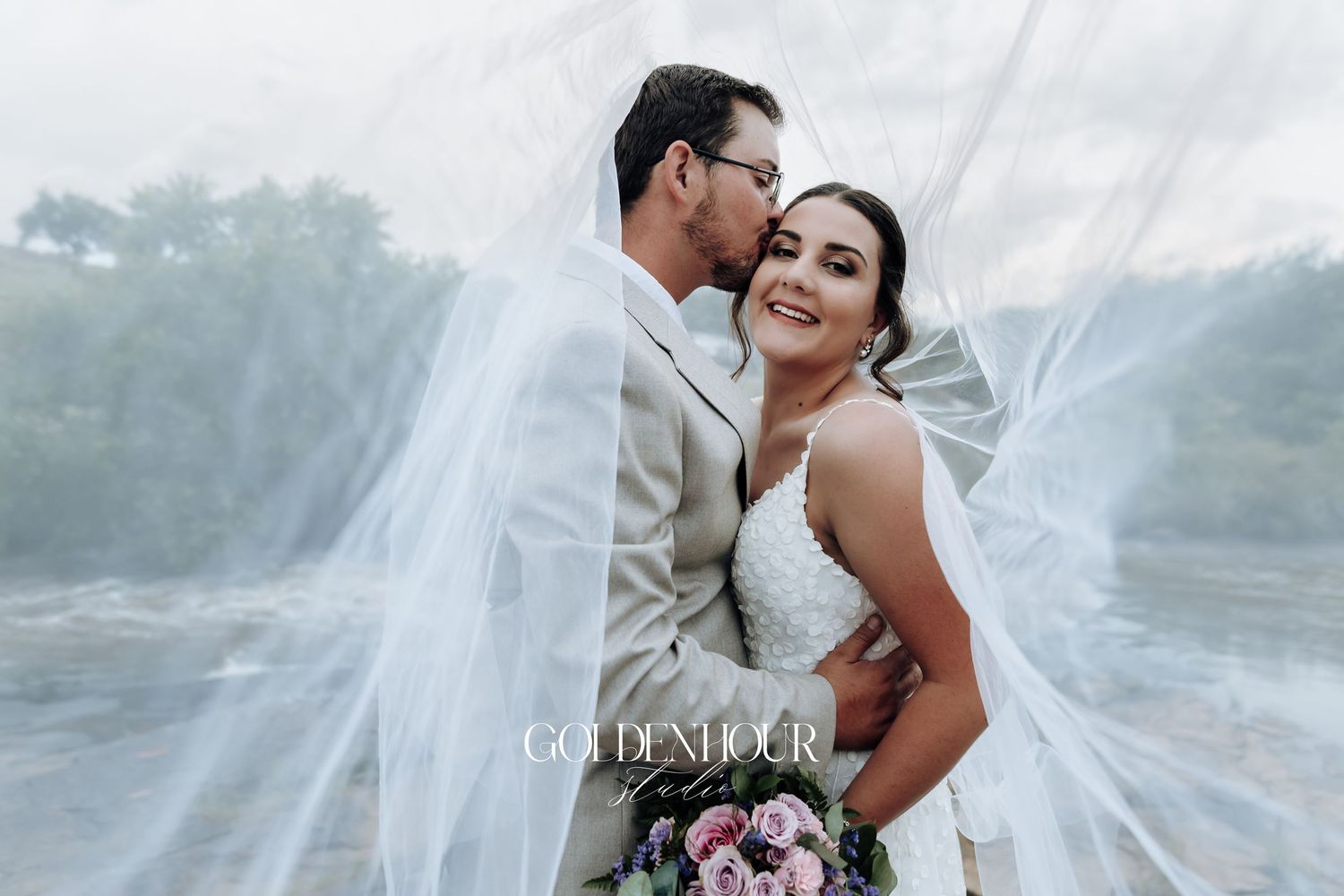 Wedding couple sharing an intimate moment with flowing veil in dramatic lighting.