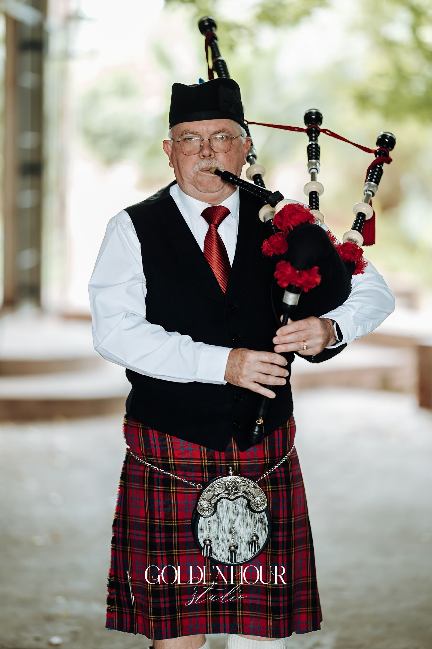 Traditional Scottish bagpiper in red tartan kilt performing at an outdoor wedding ceremony.