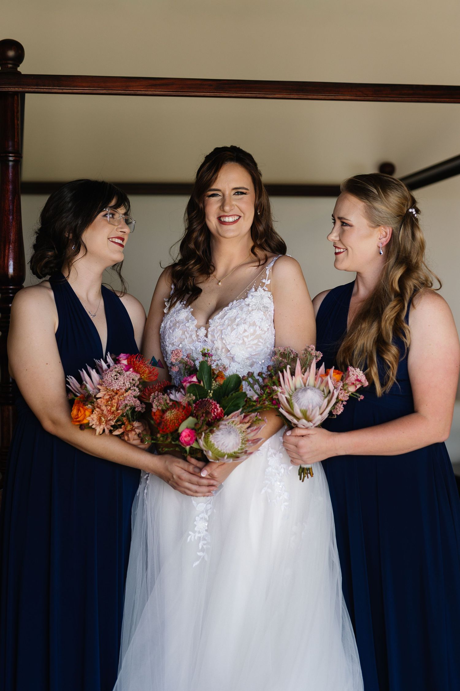 Wedding party members in navy blue dresses and white gown share joyful moments while holding colorful bouquets.