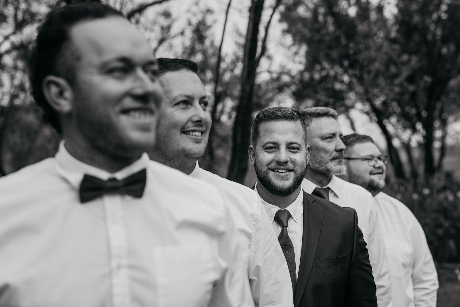 Black and white photo of groomsmen lined up and smiling during an outdoor wedding celebration.