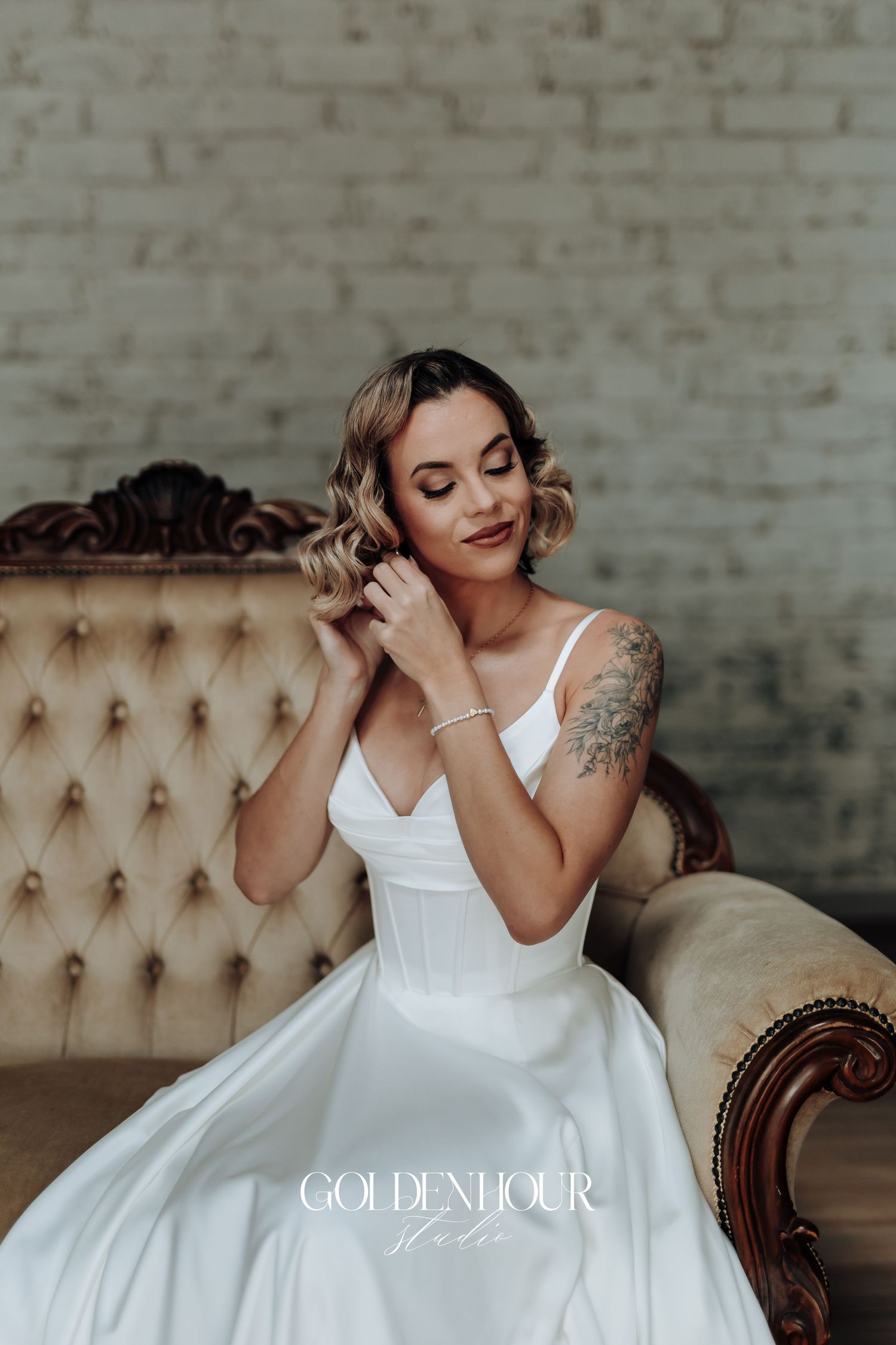 Bride in elegant white wedding gown posing on vintage tufted furniture.
