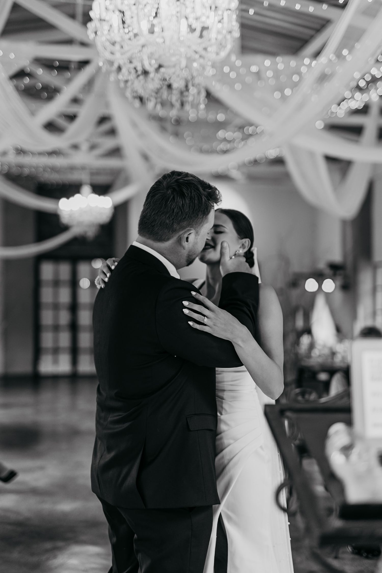A romantic black and white photo series of a couple sharing their first dance at a wedding reception under crystal chandeliers.