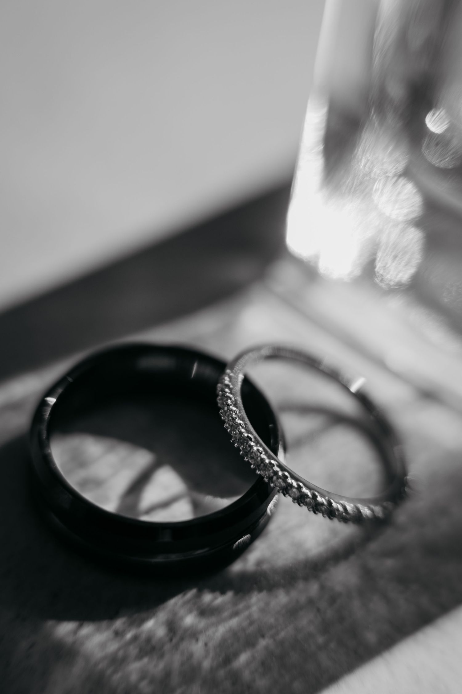 Black and white photo of two wedding rings, one smooth dark band and one textured silver band, resting on a surface.