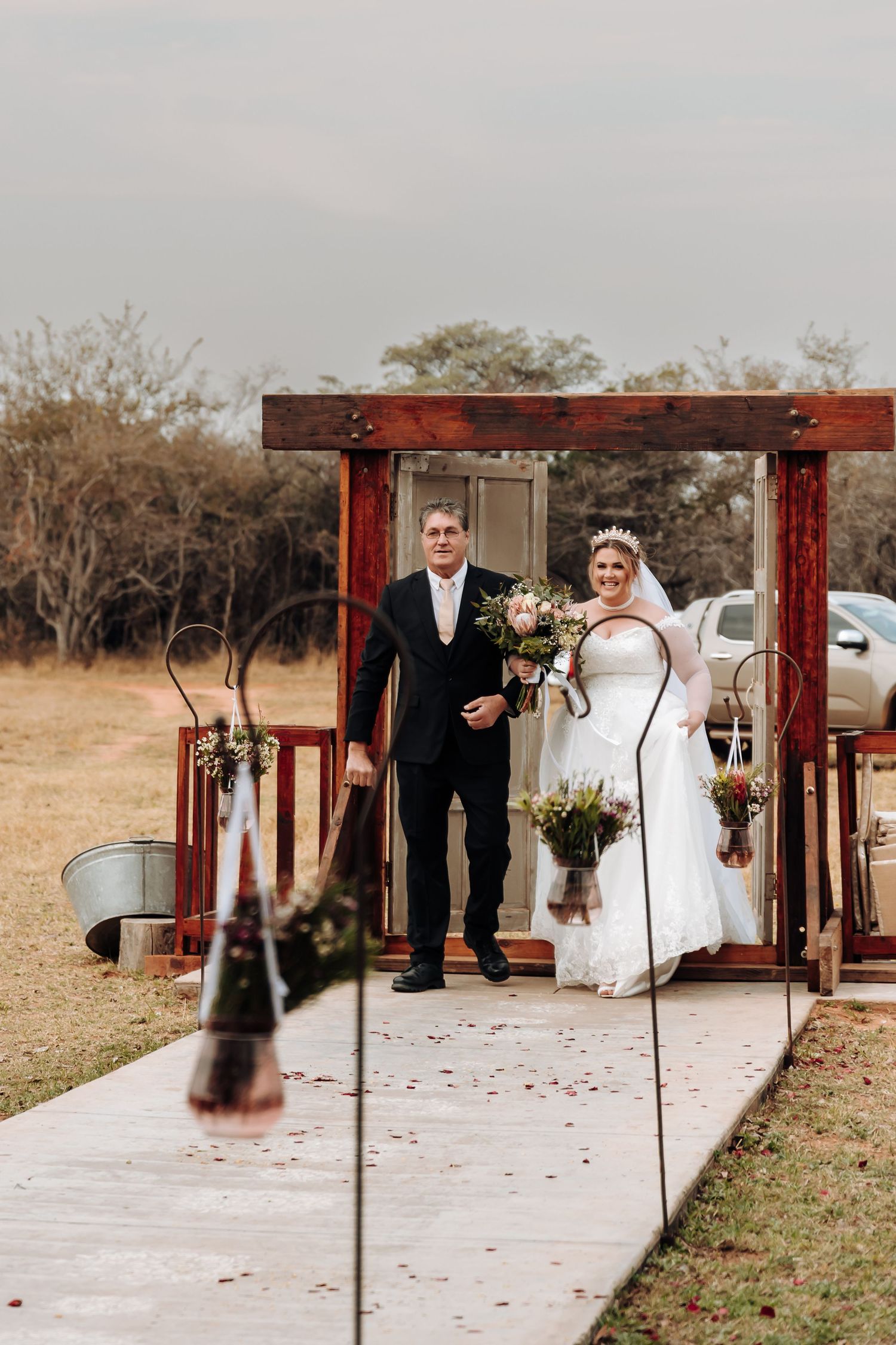 A wedding ceremony scene with a rustic wooden arch decorated with floral arrangements and rustic metal accents.