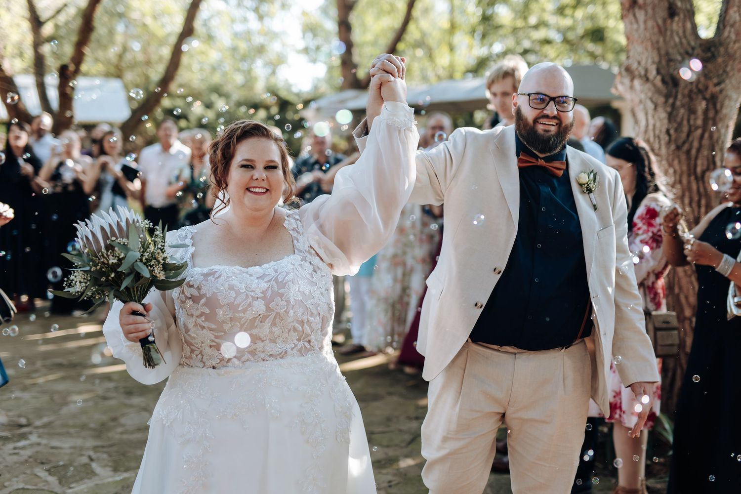 Joyful wedding guests dancing and celebrating together at an outdoor reception under string lights and trees.