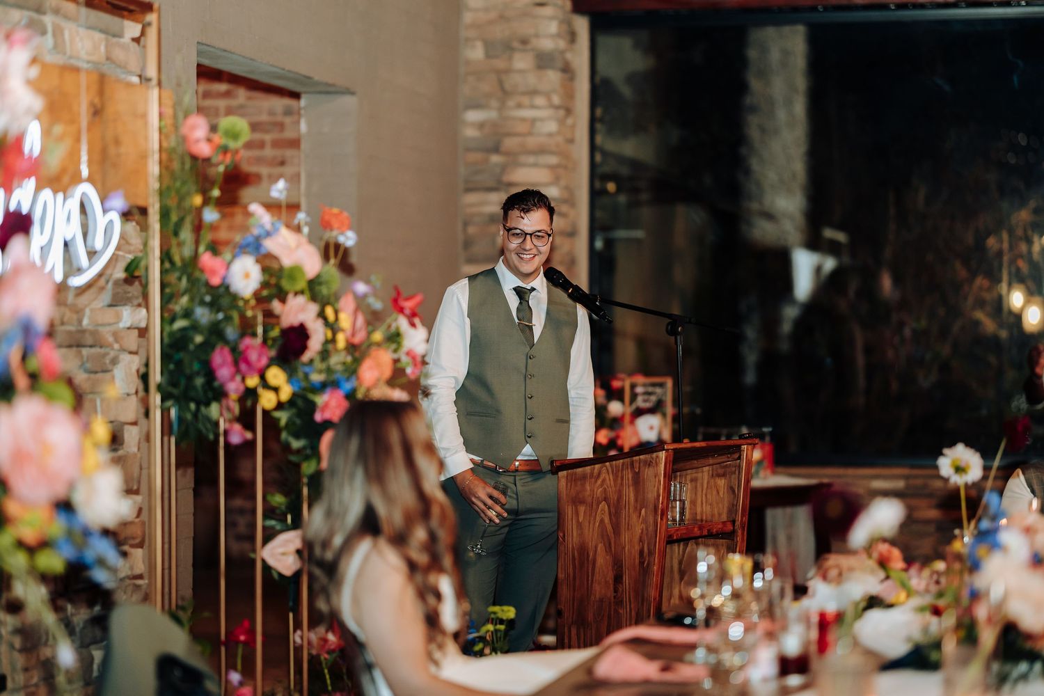 Wedding reception venue decorated with floral arrangements against exposed brick walls and warm lighting.