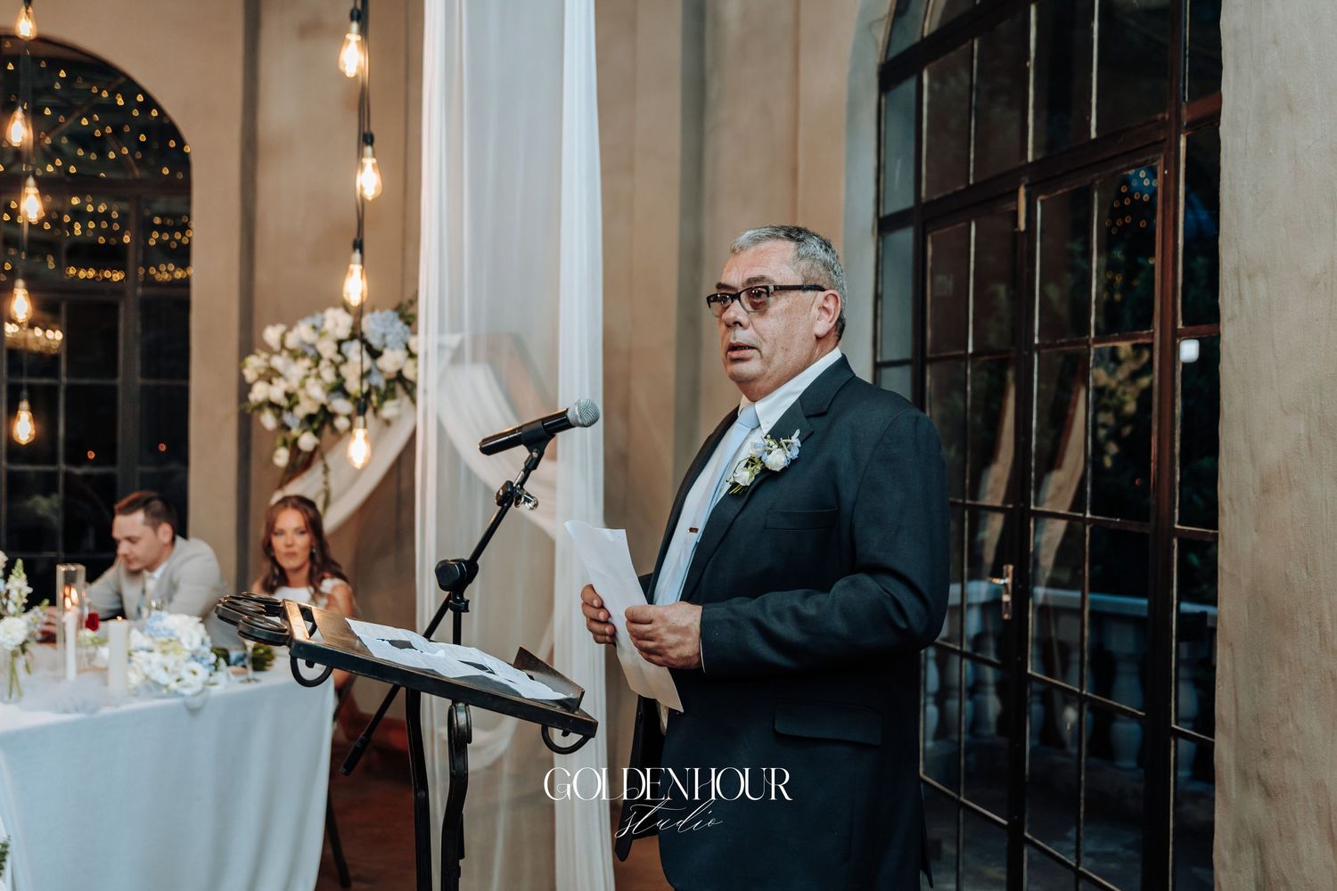 Speaker delivering a speech at an elegant indoor wedding reception with floral decorations.