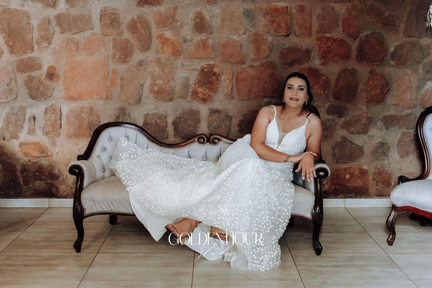 Elegant bridal portraits on vintage furniture against a rustic stone wall.