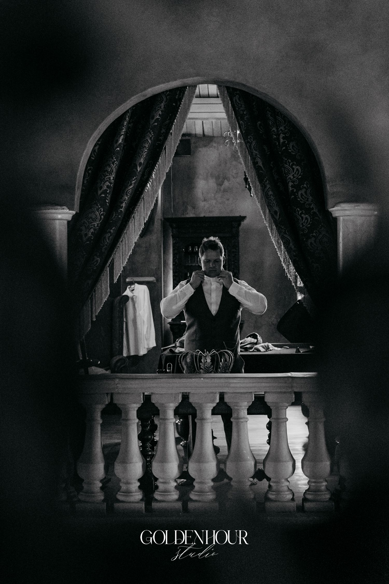 Groom preparing in elegant arched mirror reflection, black and white wedding photography.