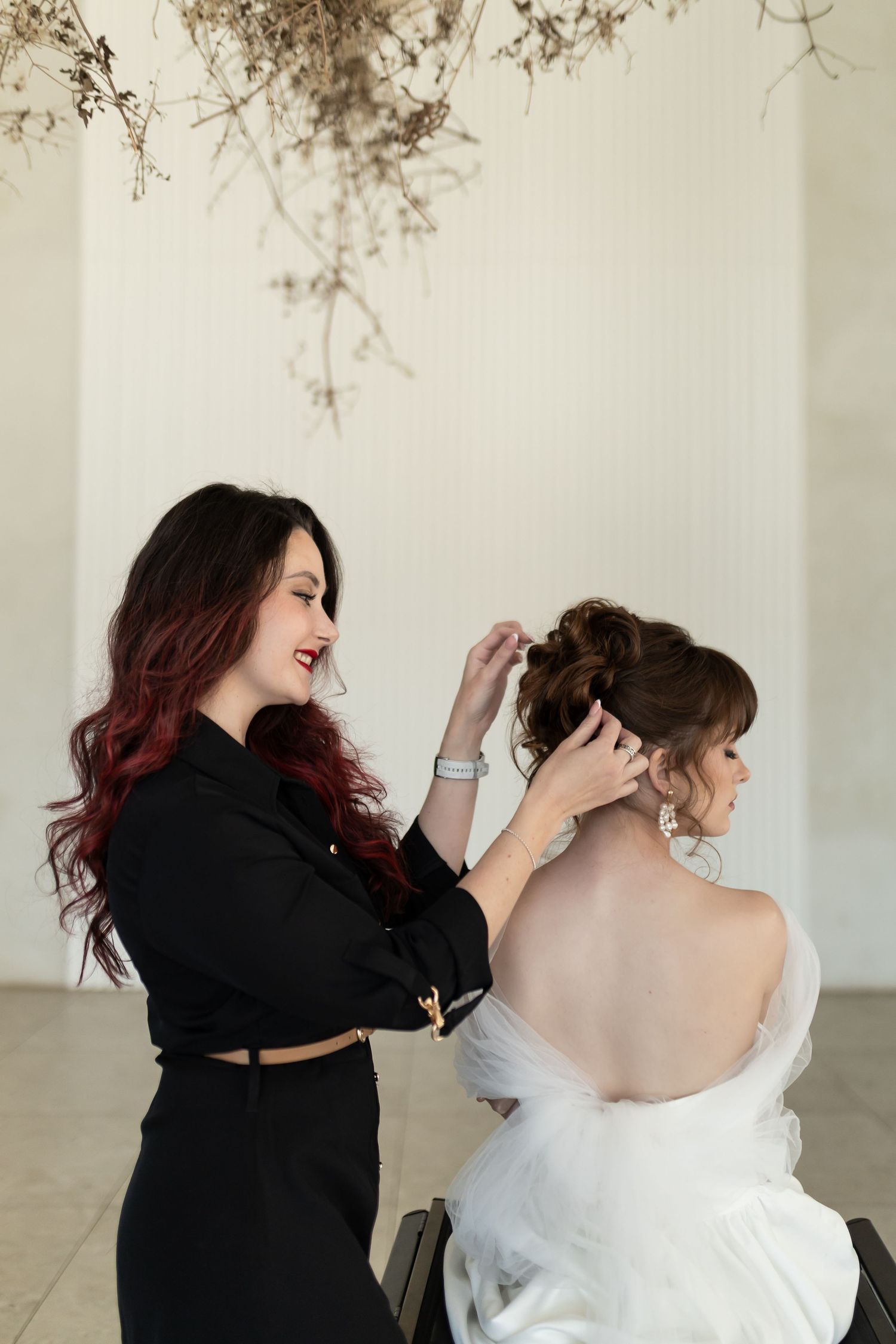 A hairstylist in black applies finishing touches and hairspray to complete a bridal hairstyle.