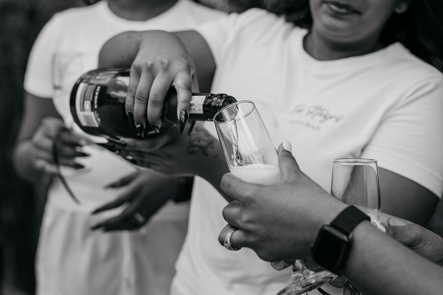 Black and white photo of hands pouring champagne into glasses at celebration.