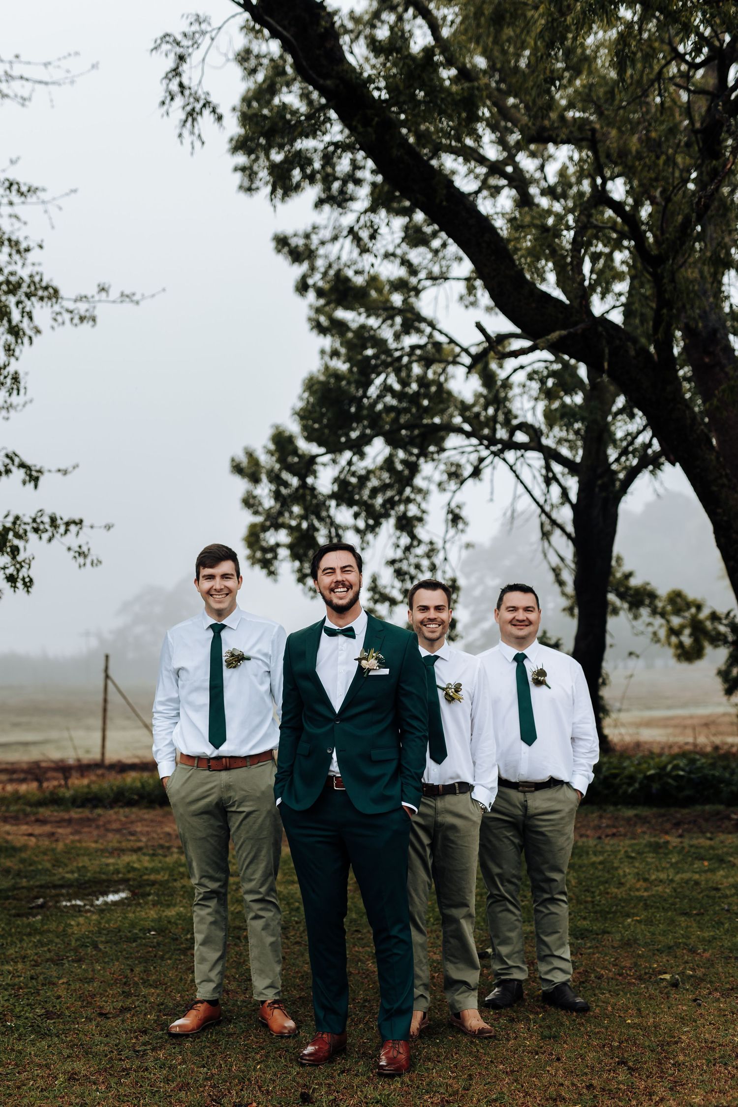 Wedding party poses outdoors with the groom in emerald suit and groomsmen in white shirts and green ties.