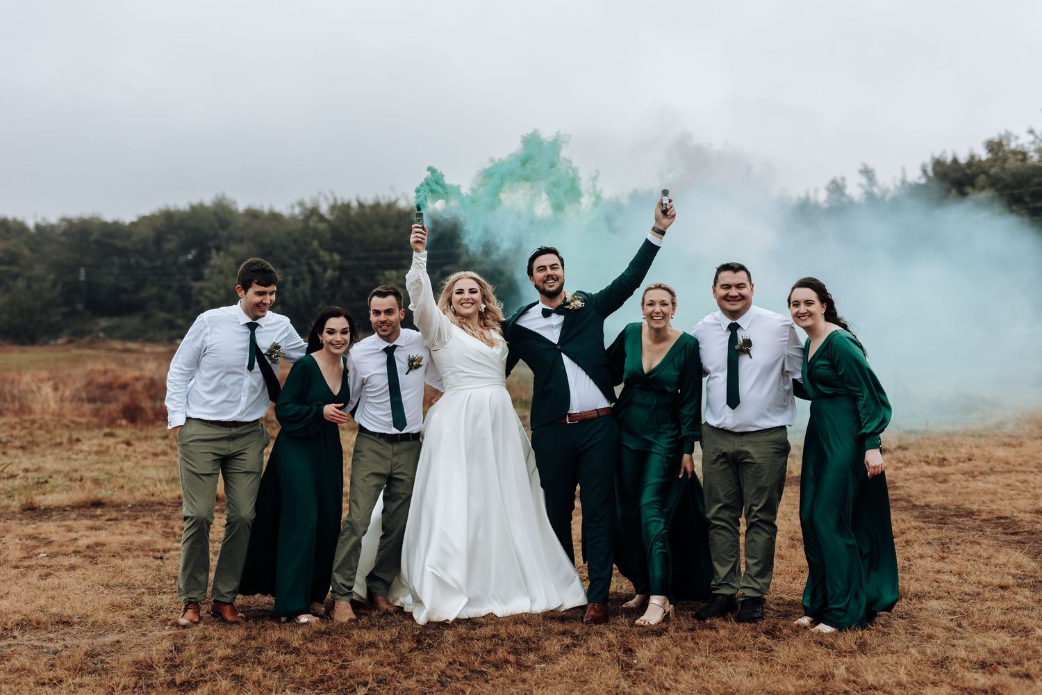 Wedding party celebrates with teal smoke bombs in a rustic outdoor setting.