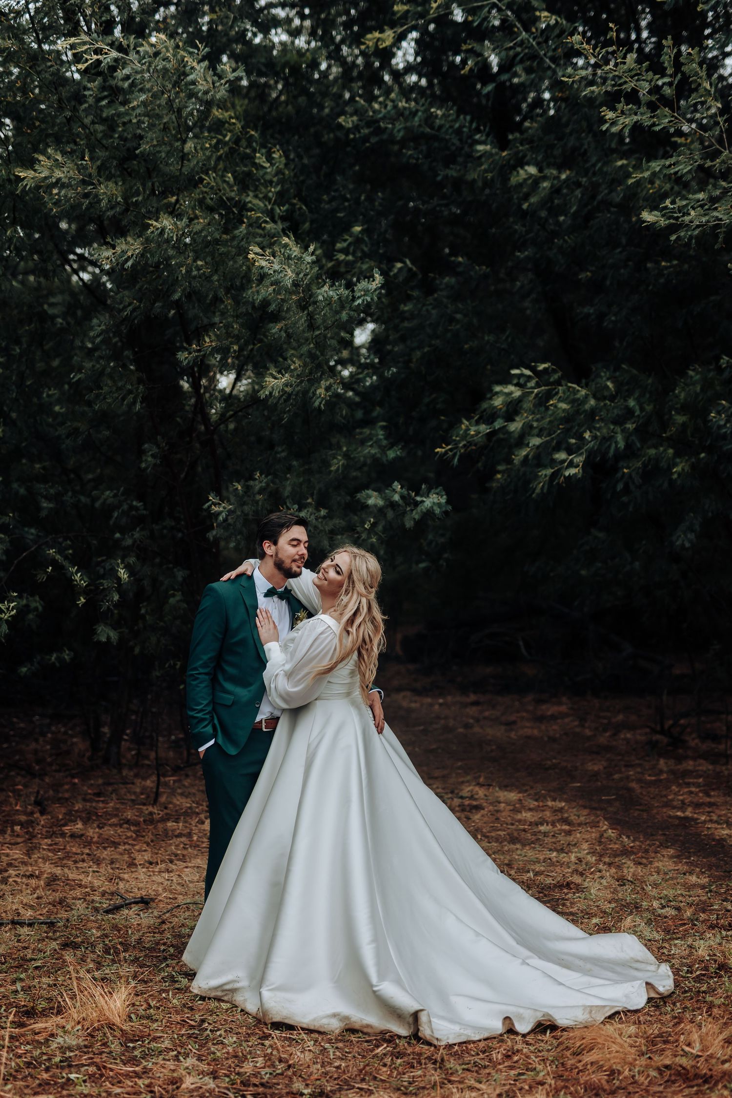 An intimate wedding portrait captured against a backdrop of lush forest greenery.