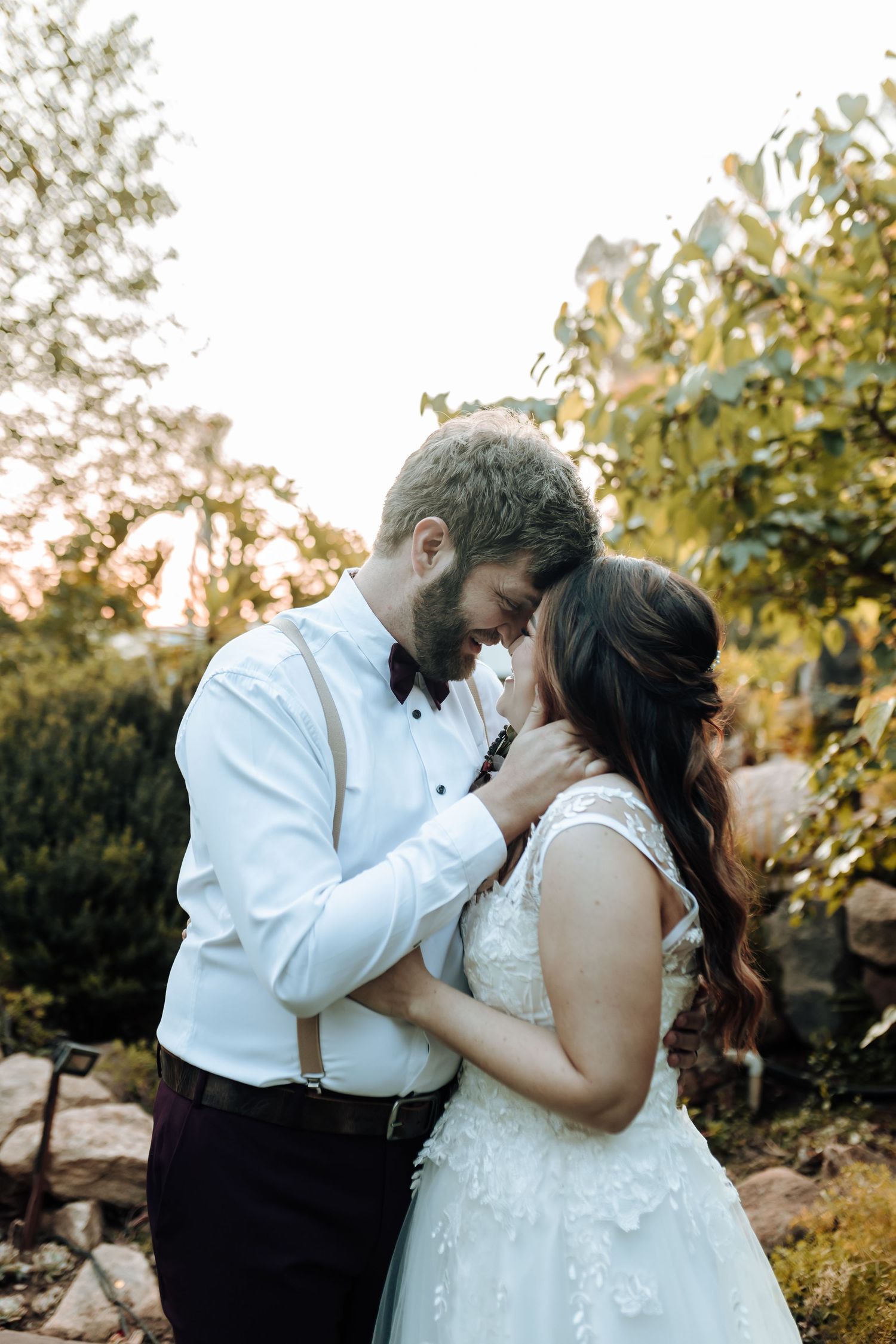Intimate wedding portrait of couple embracing against garden backdrop at sunset.