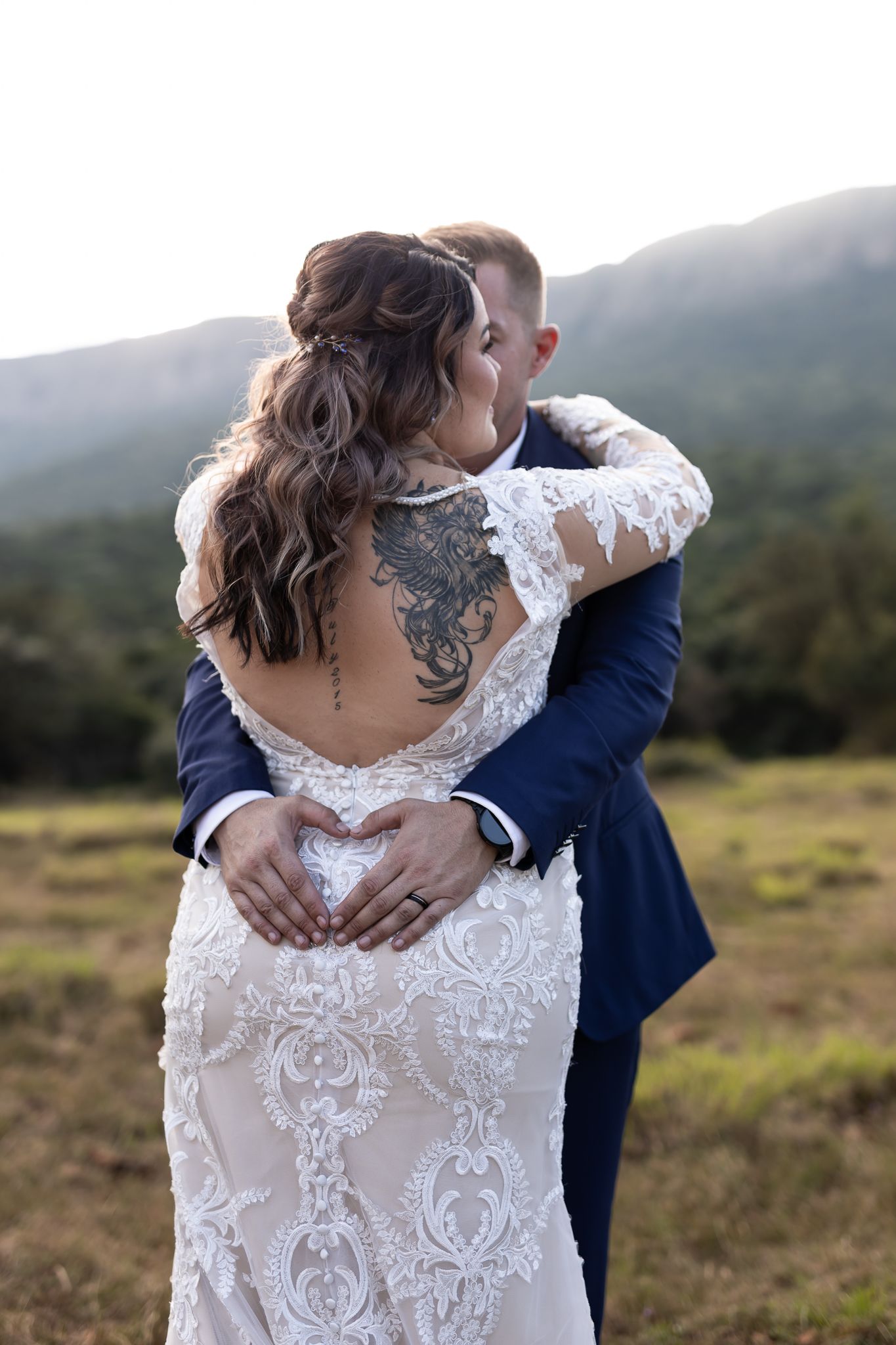 Back view of bride in lace dress embracing groom showing intricate dress detail.