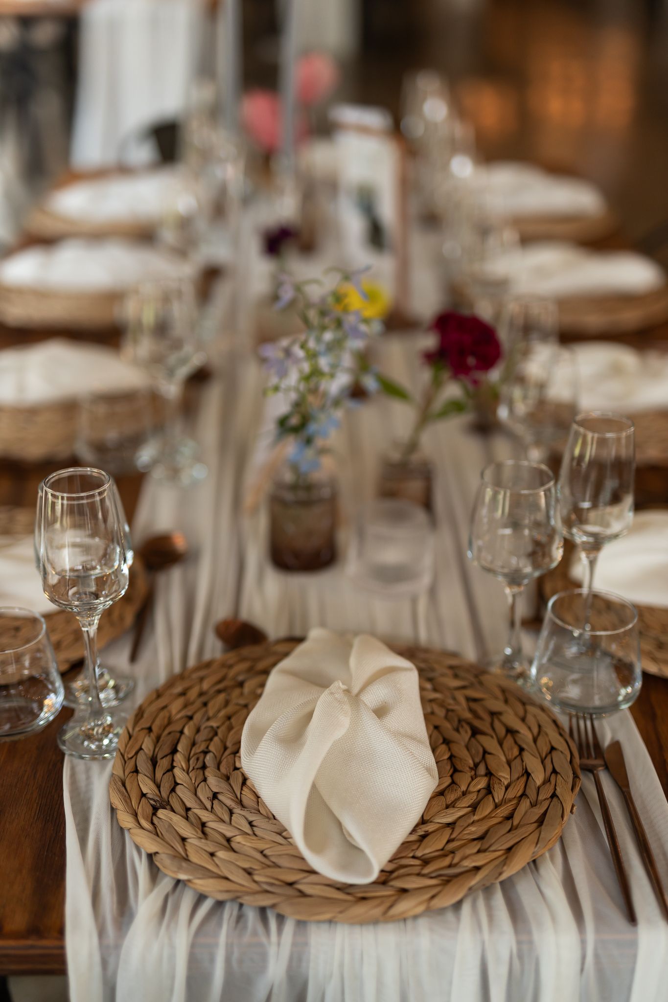 Rustic place setting with woven charger plate, white napkin, and delicate floral accents.