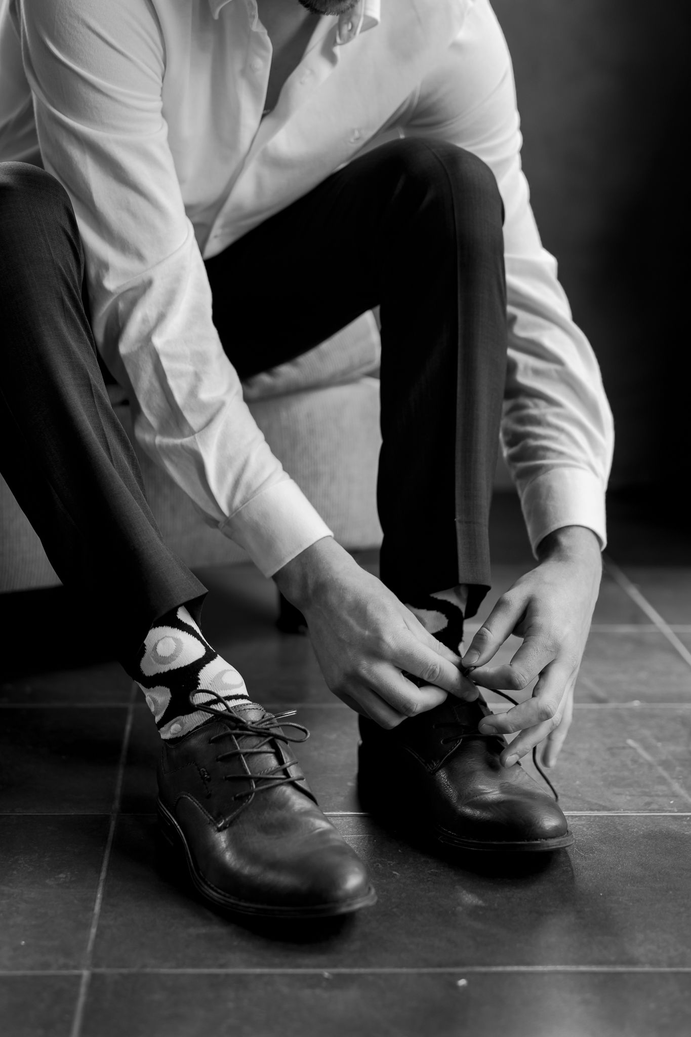 Close-up of dress shoes being tied on tile floor in black and white.