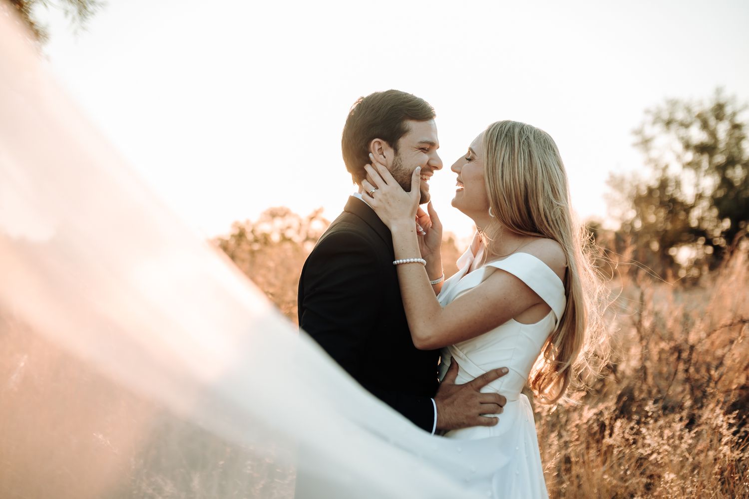 Candid wedding photo of couple embracing in a sun-drenched field.