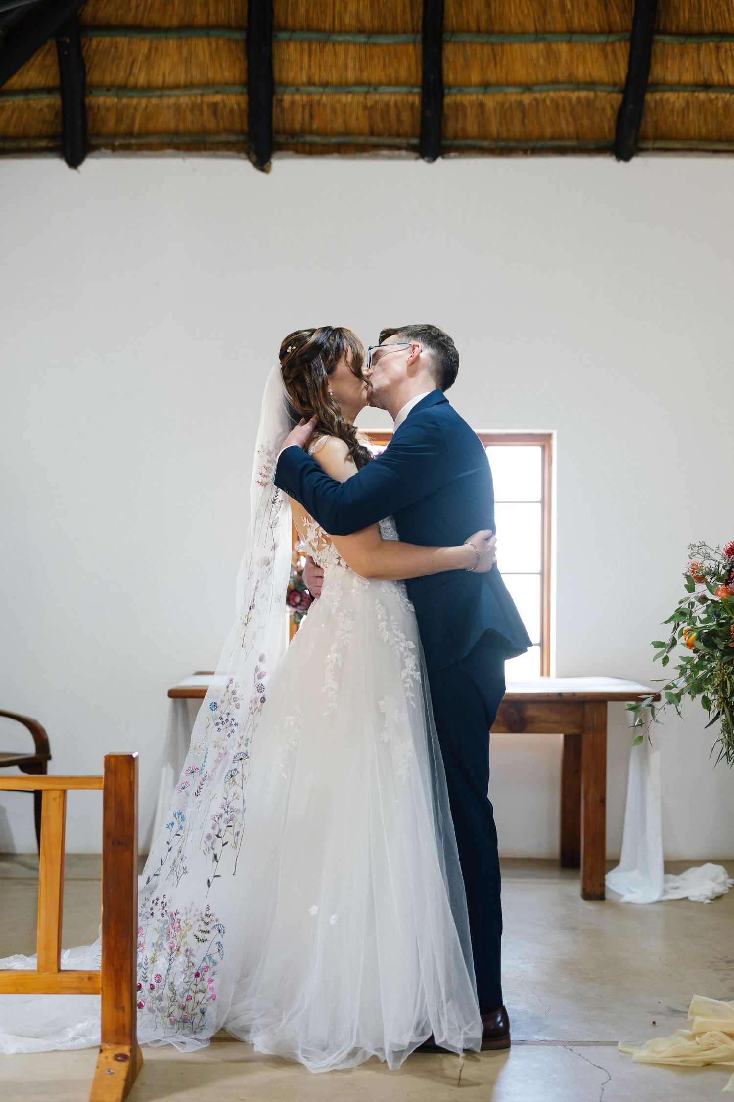 A romantic wedding moment captured as the couple shares a tender kiss under a thatched roof venue.