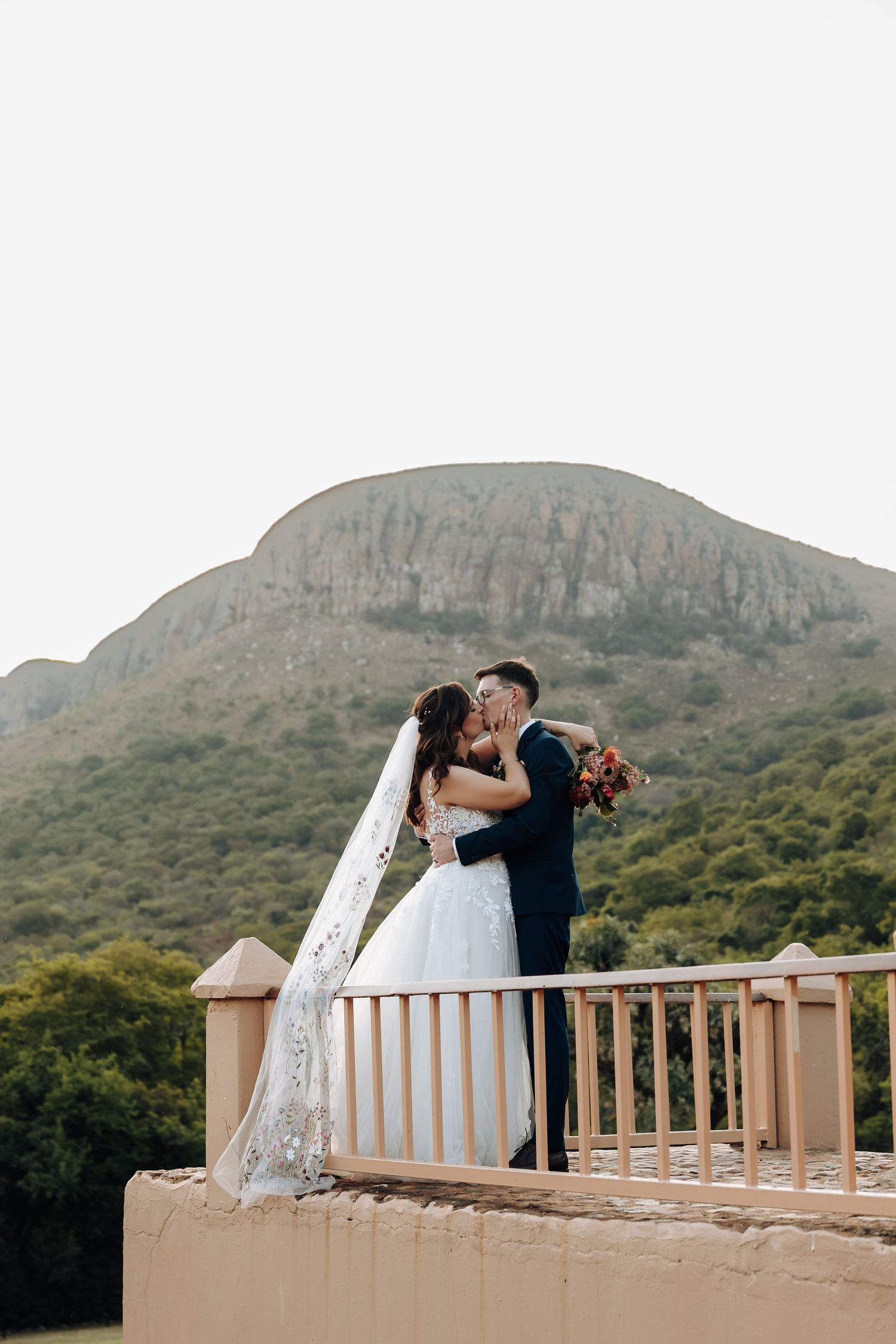 A couple shares a romantic moment on a balcony overlooking scenic mountain landscapes.