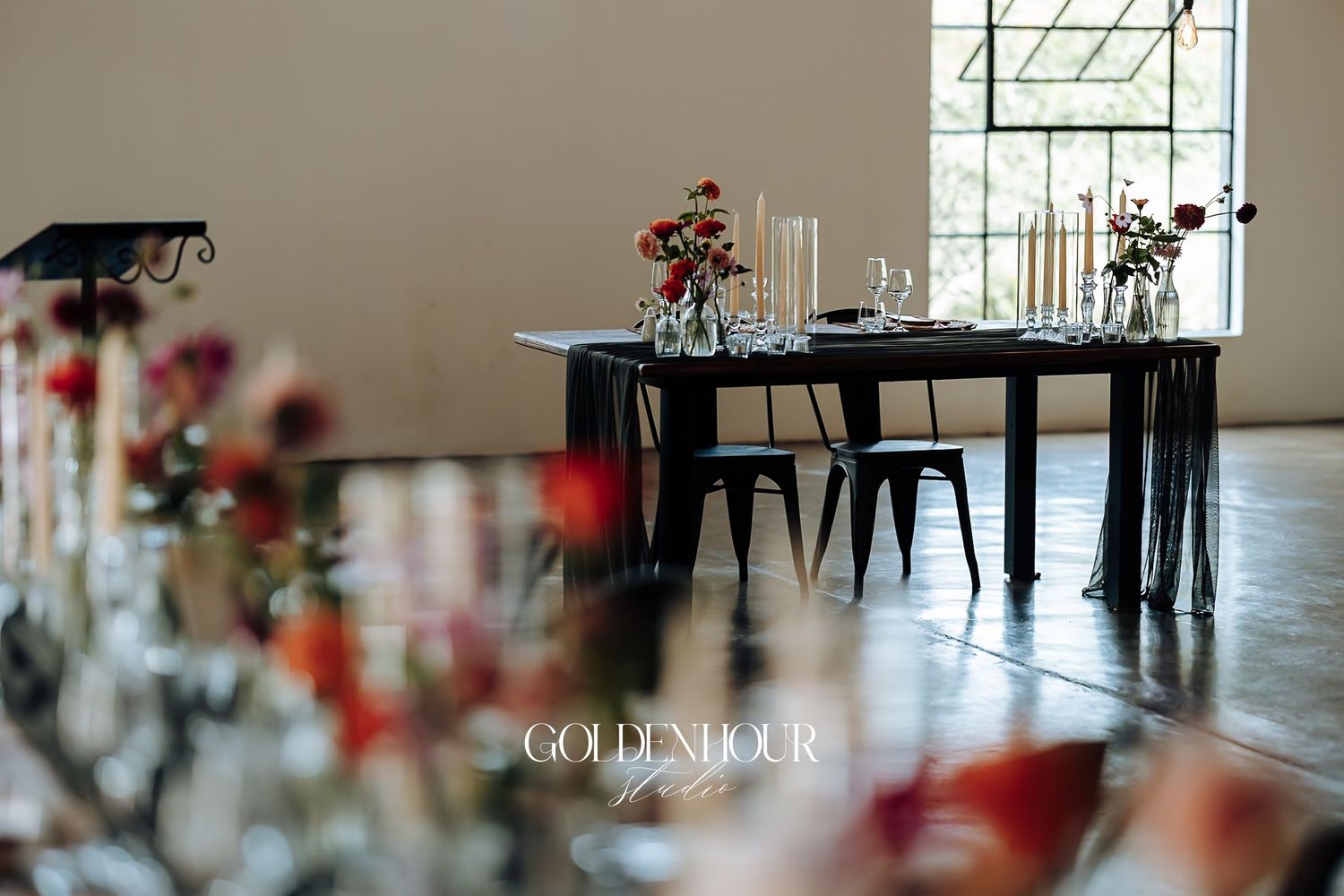 Elegant wedding reception setup with black tables, floral centerpieces, and soft lighting in a modern venue.