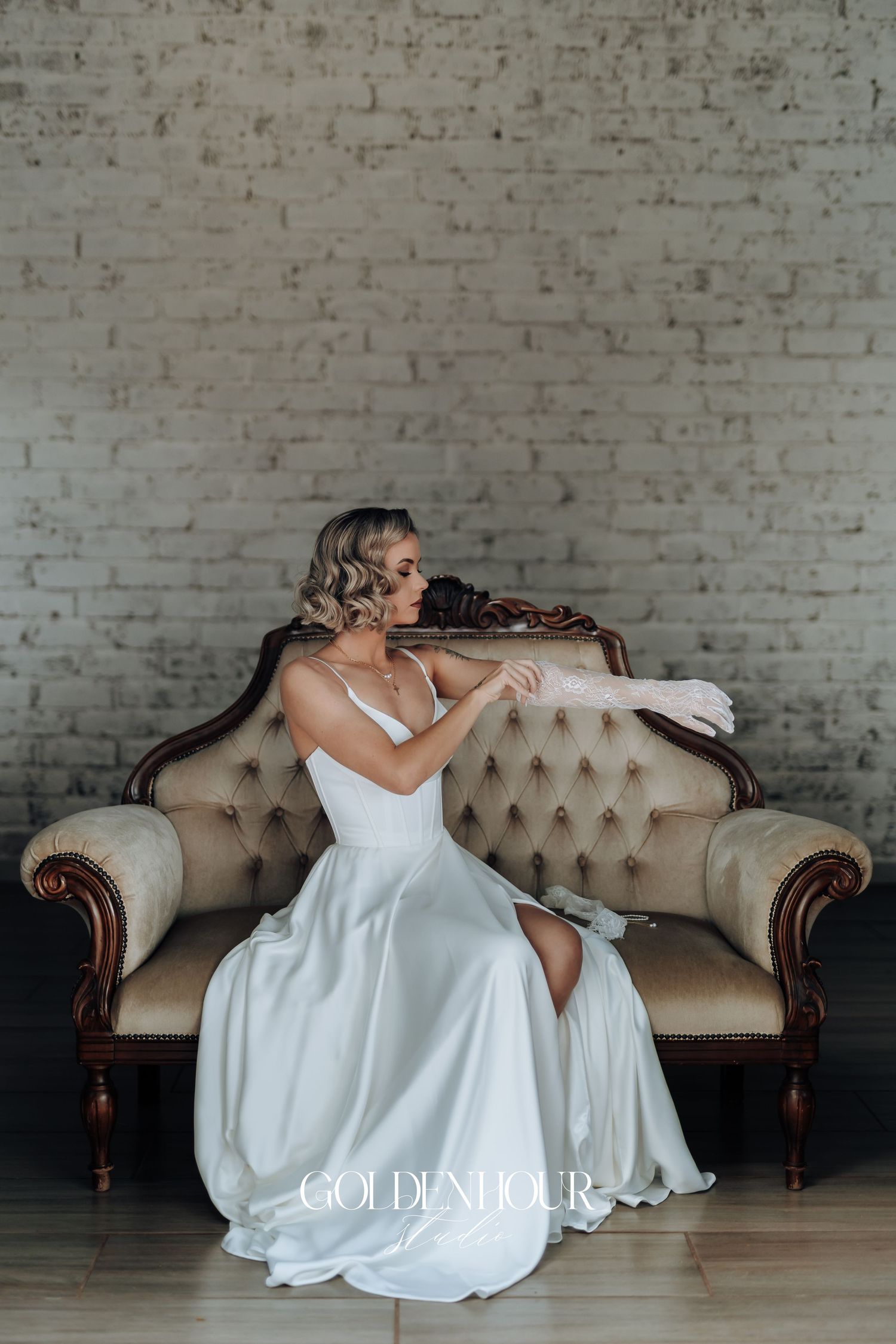 Elegant bridal party in white dresses lounging on vintage tufted sofa.