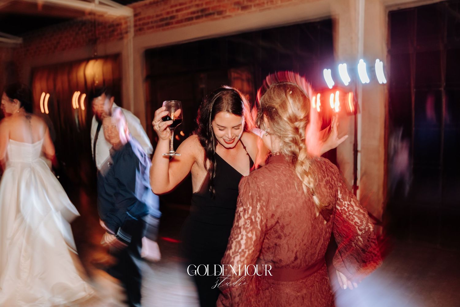 Guests dancing joyfully at a wedding reception with colorful stage lights in a rustic brick venue.
